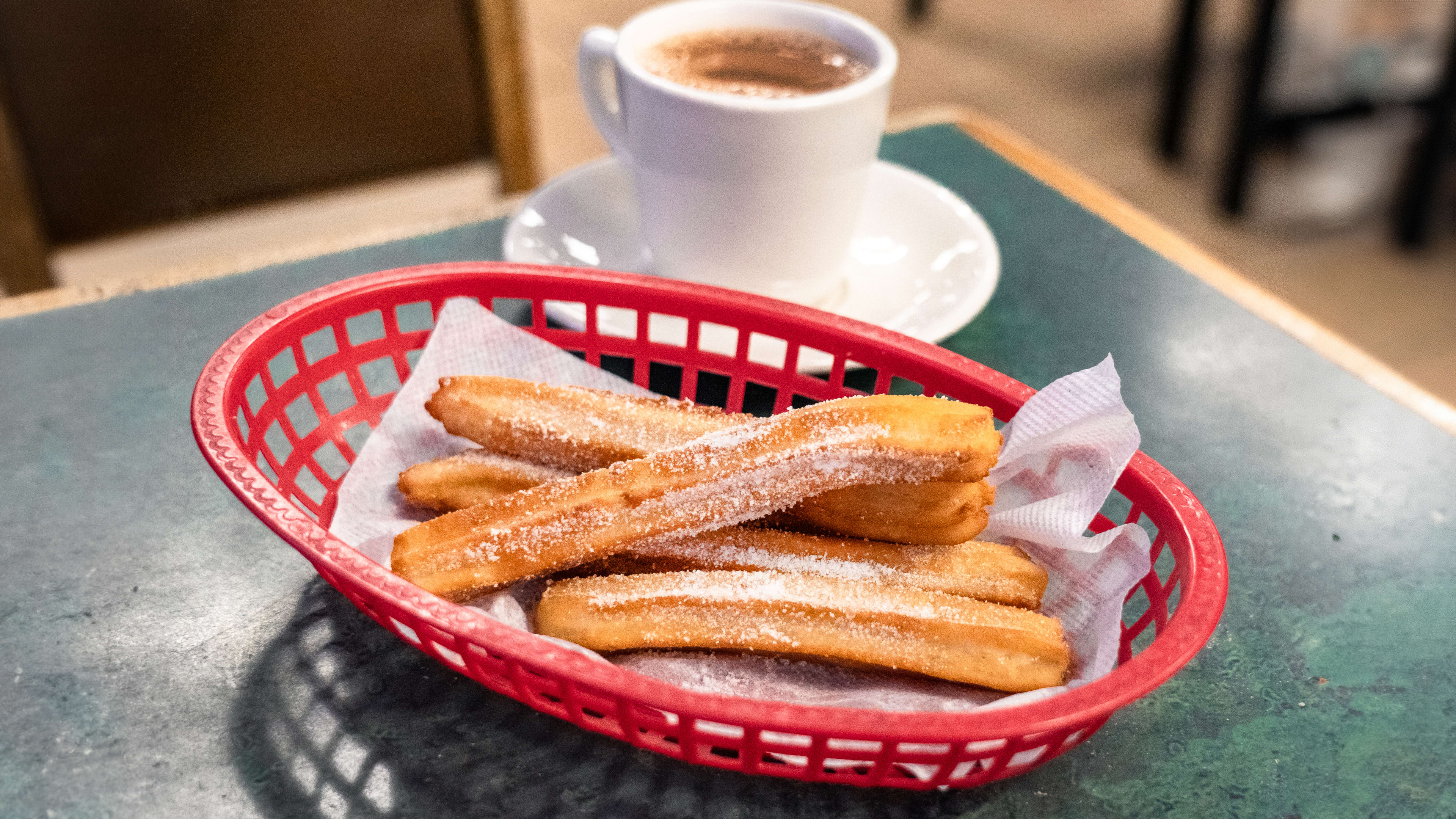 Plastic basket of churros with a mug of hot chocolate