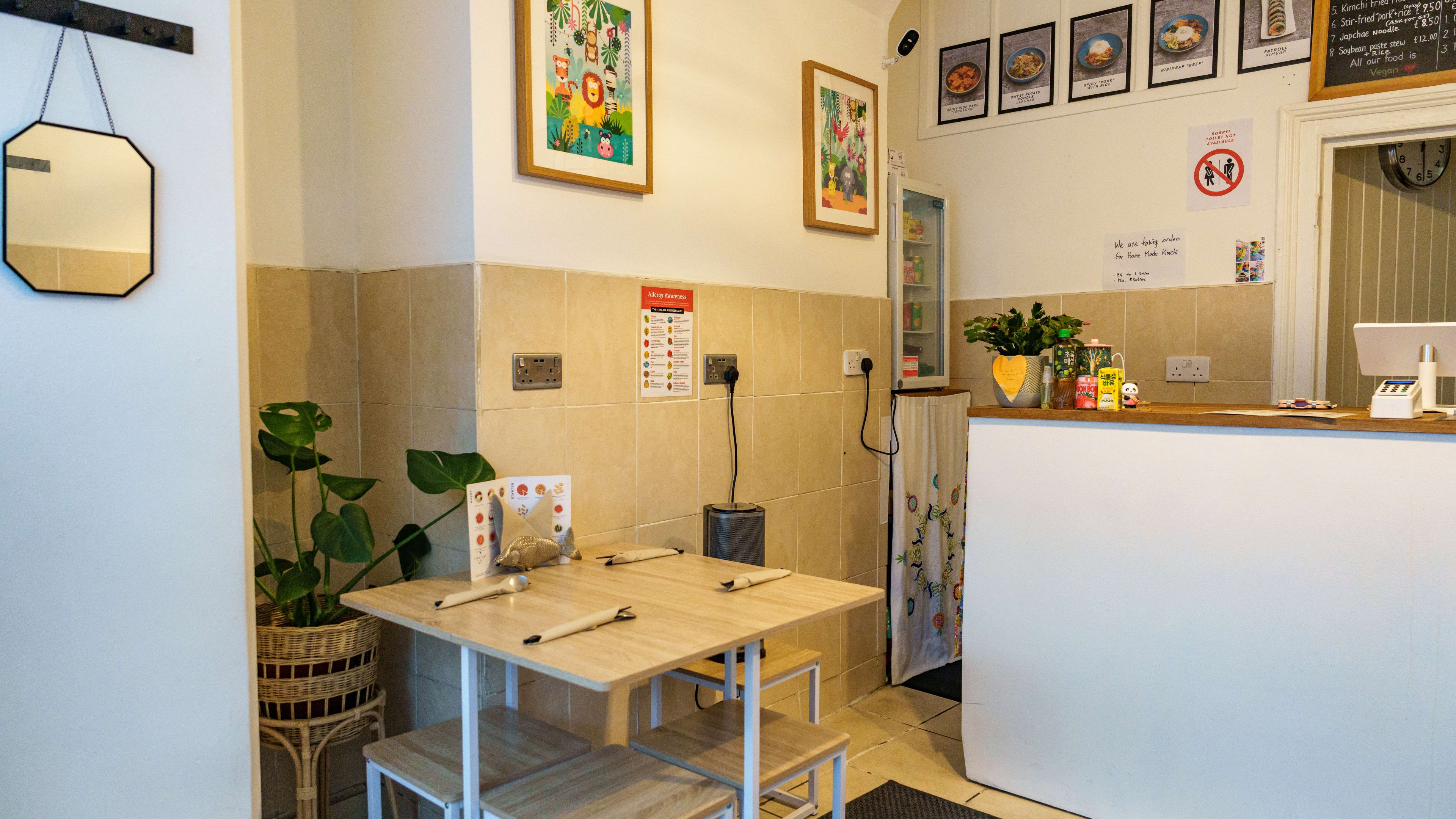 White and beige interior of Mukbap, with a small wooden table with stools and the front counter to the right