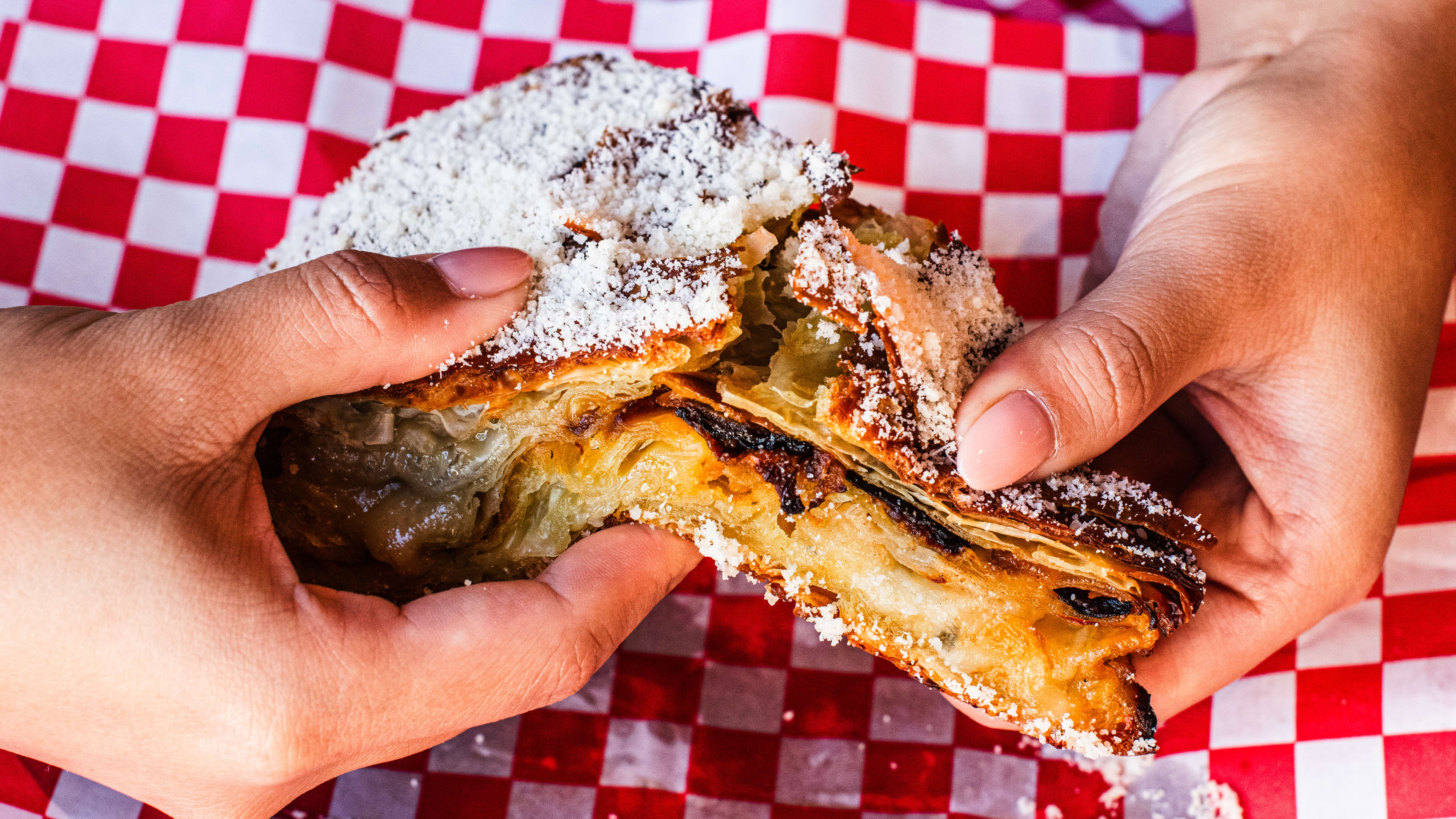 Person ripping apart the gorgonzola dolce, squash jam & pomegranate onions burek slice.