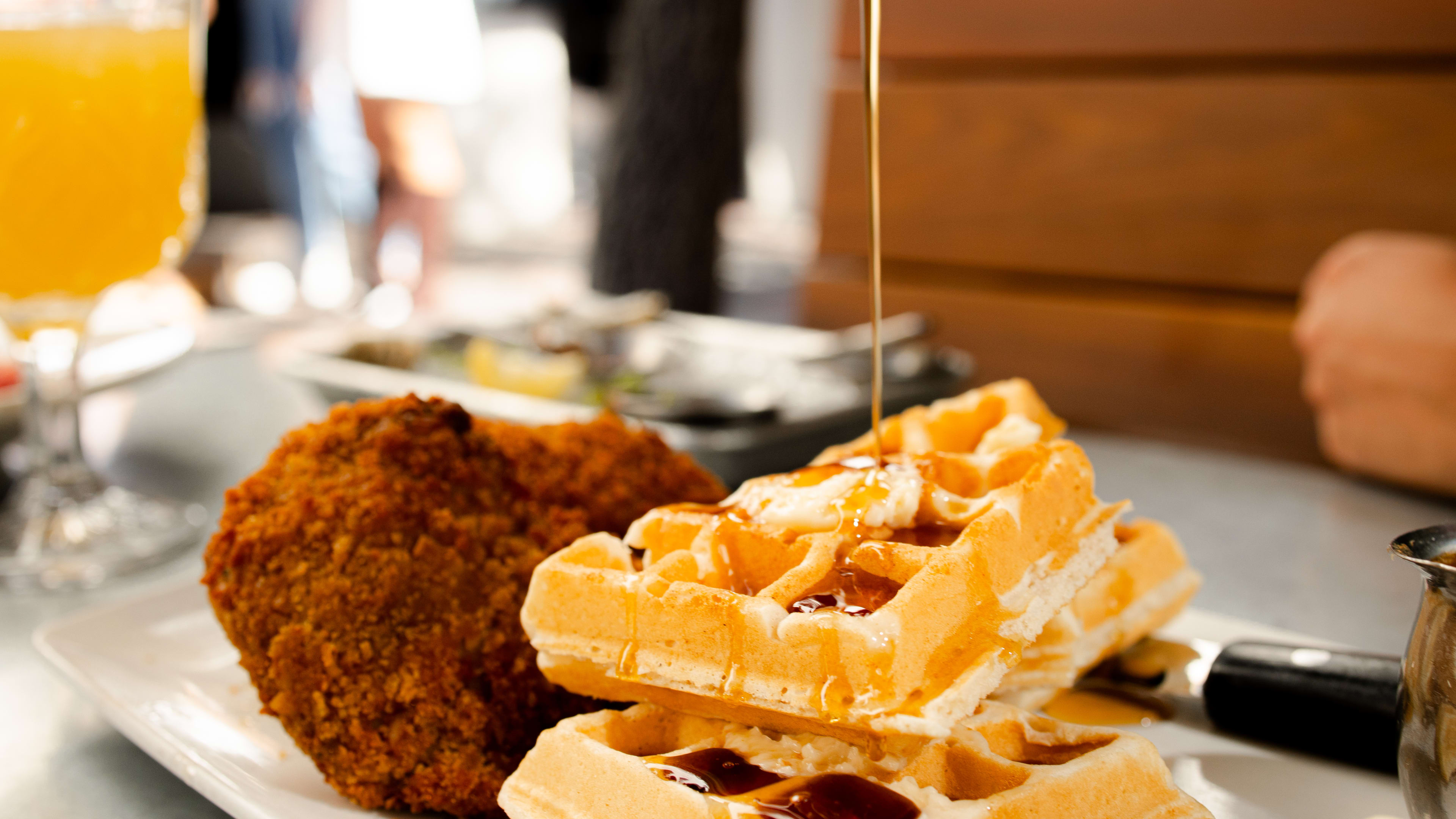 Someone pours syrup on chicken and waffles at Nola