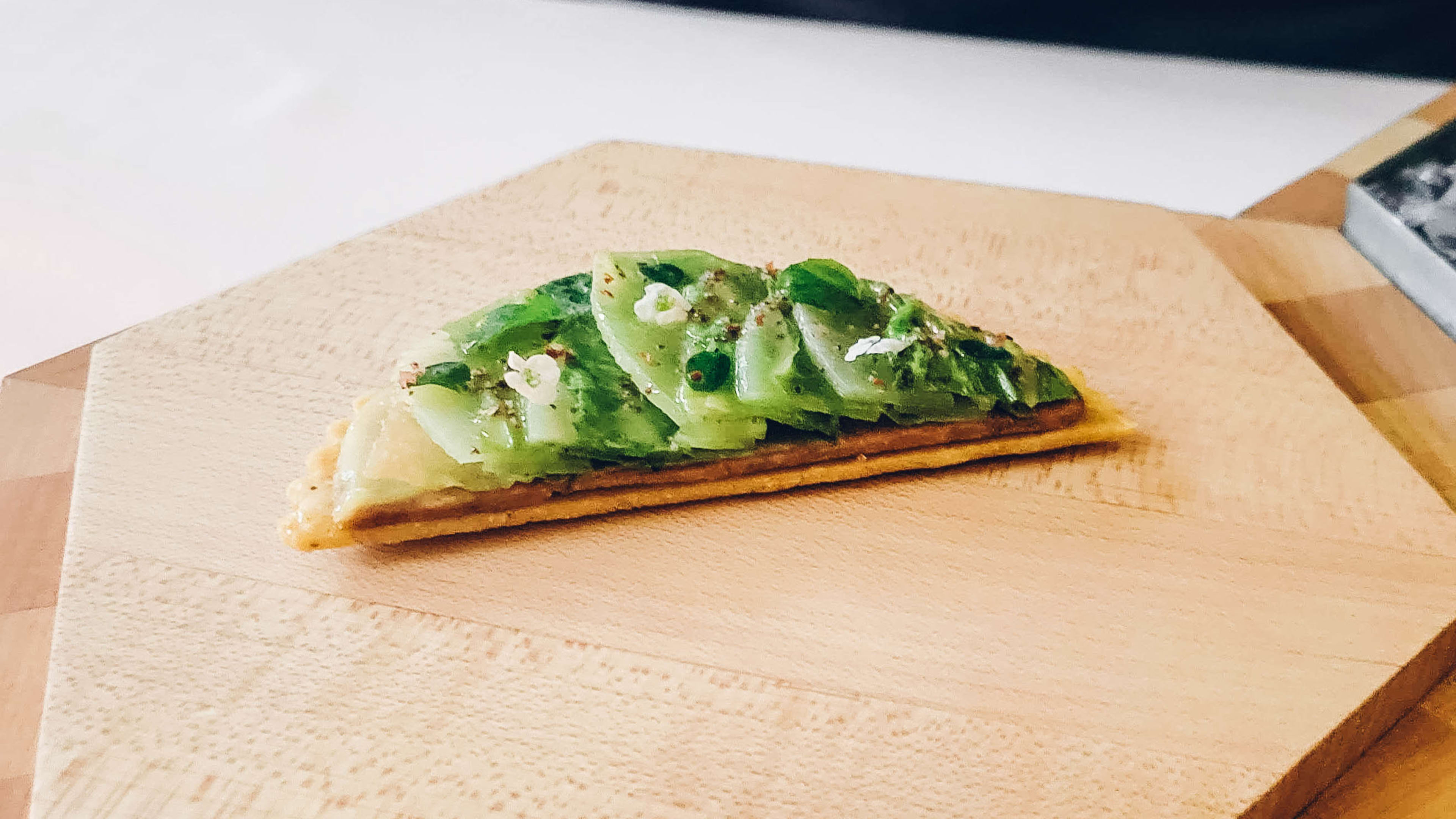 Half a tostada topped with celtuce on a big wooden block.