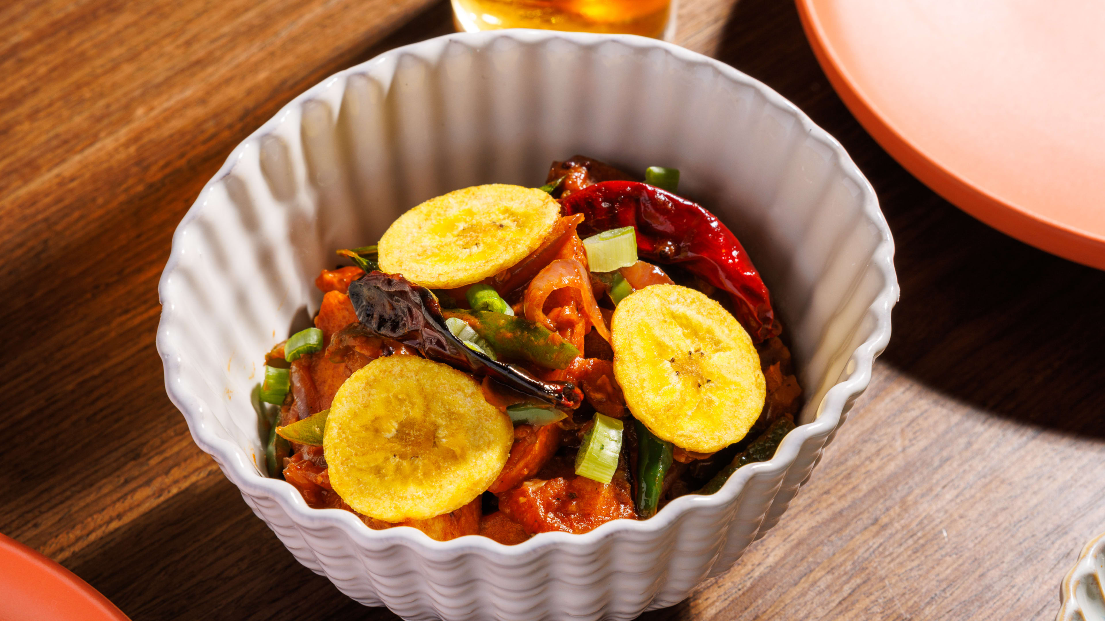 A bowl of idli topped with chilis and banana chips.