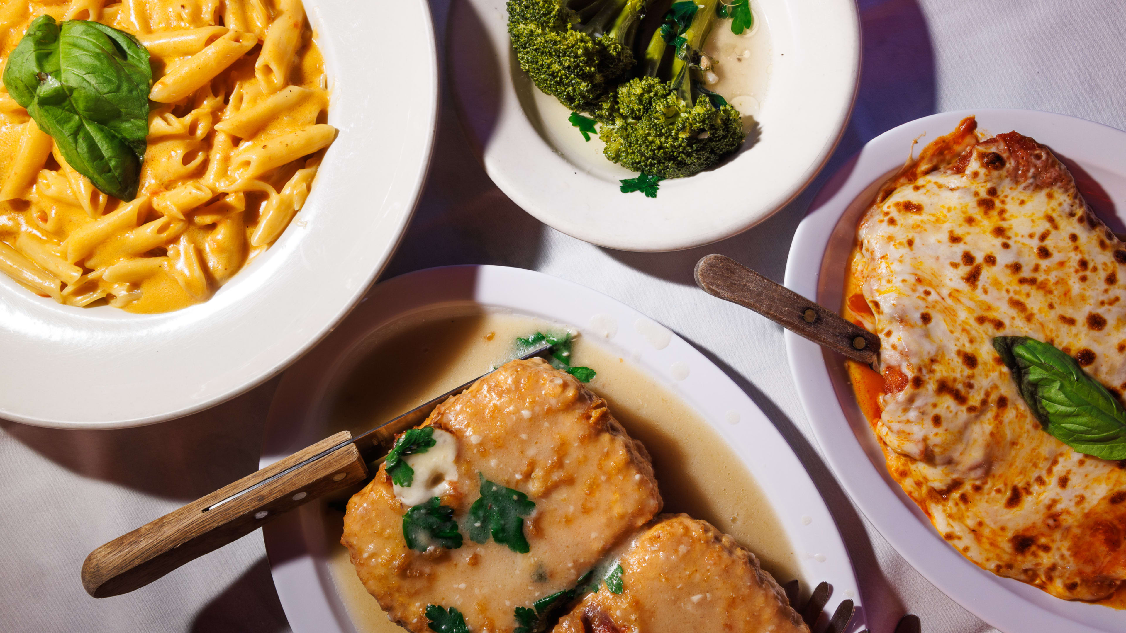 The penne alla vodka, broccoli, chicken parm, and mozzarella in carrozza from Ortobello's served on white dishes on a white tablecloth