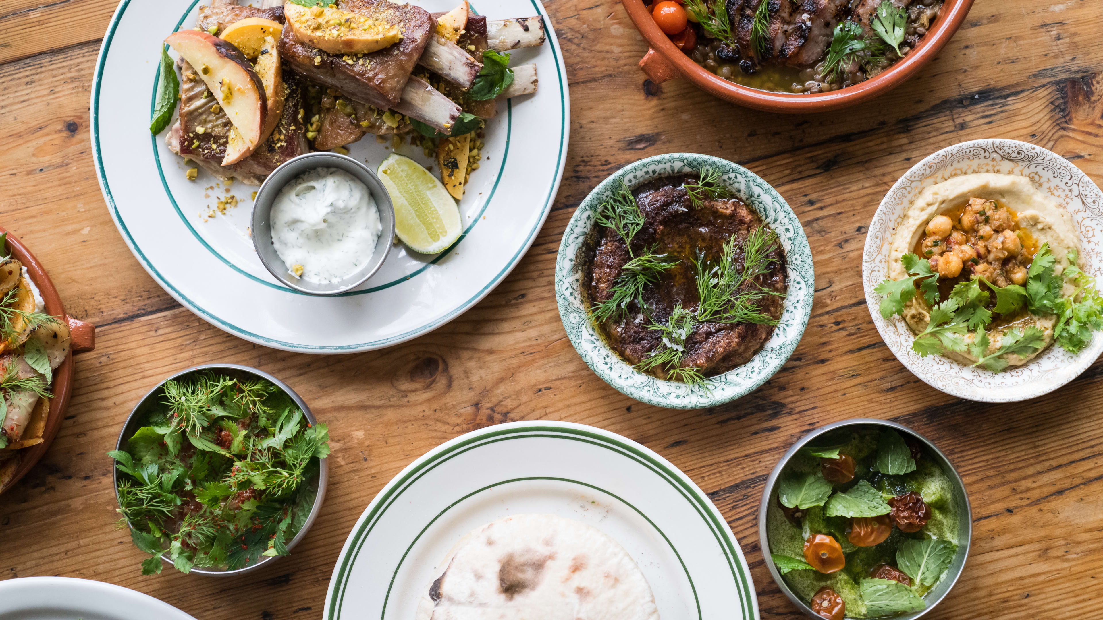 Spread of meat, dips, and pita on wooden table.