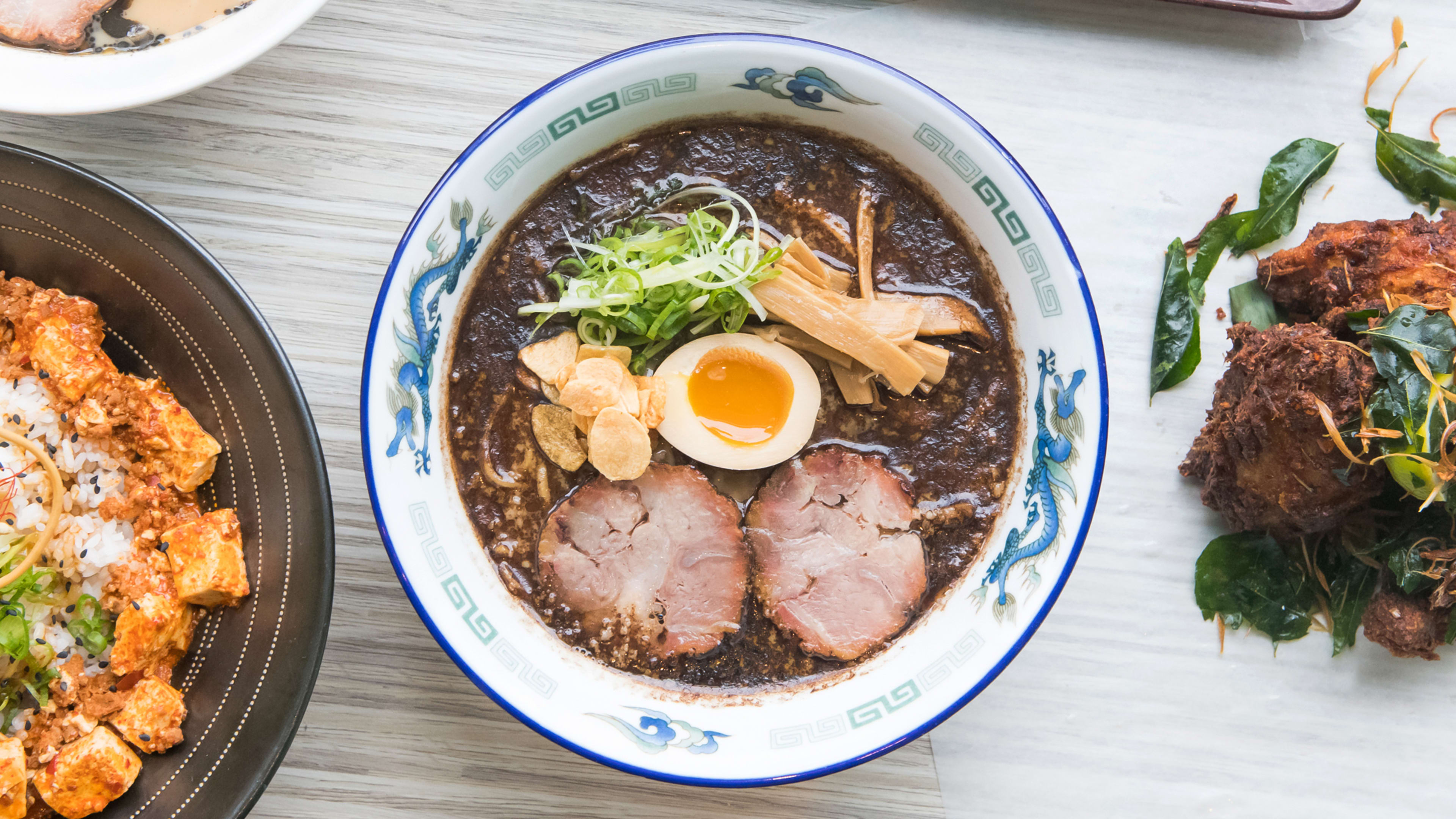 Bowl of ramen with half soft boiled egg, sliced pork, bamboo shoots, and dark broth.