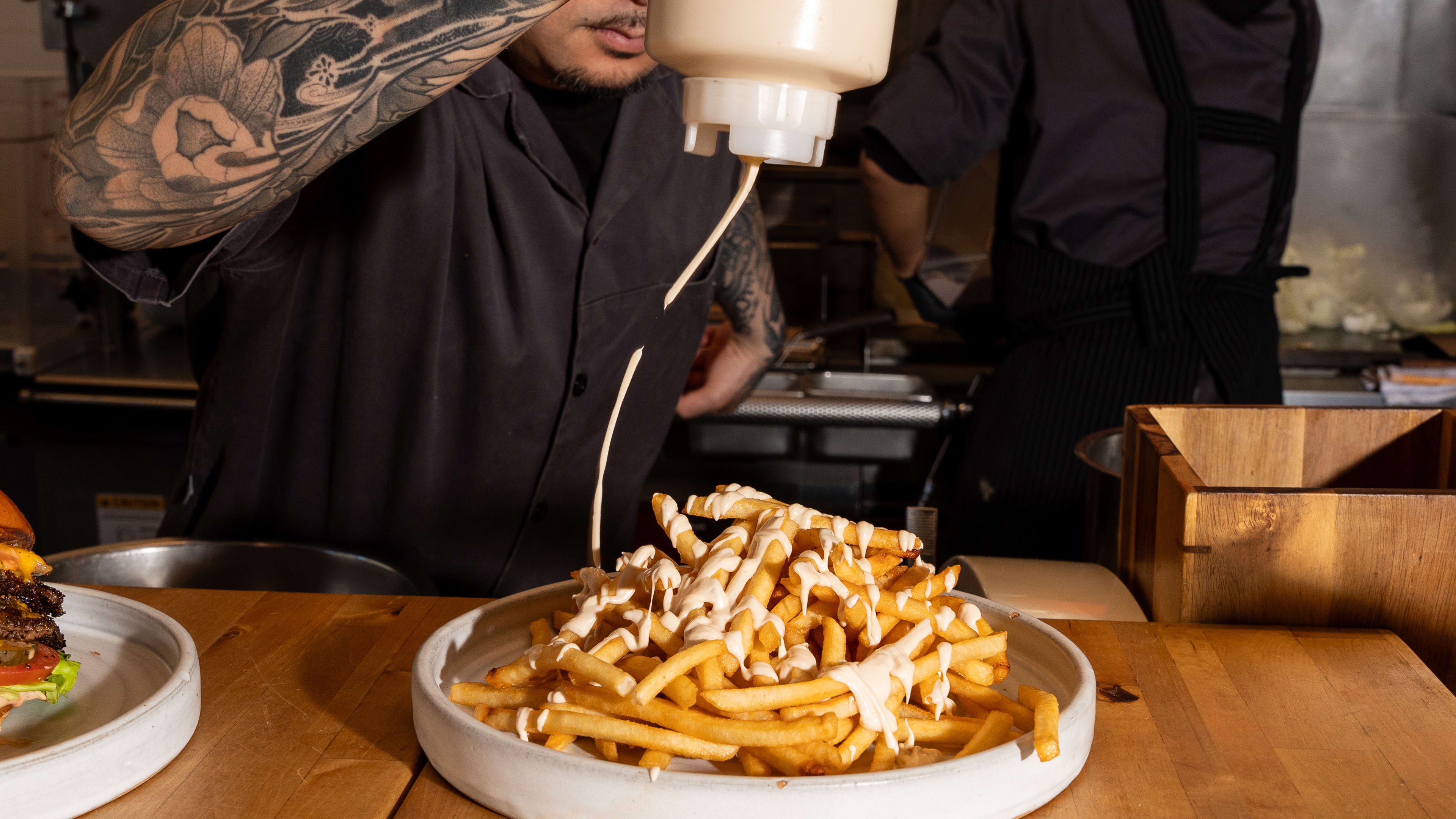 chef drizzling sauce over towering mound of fries