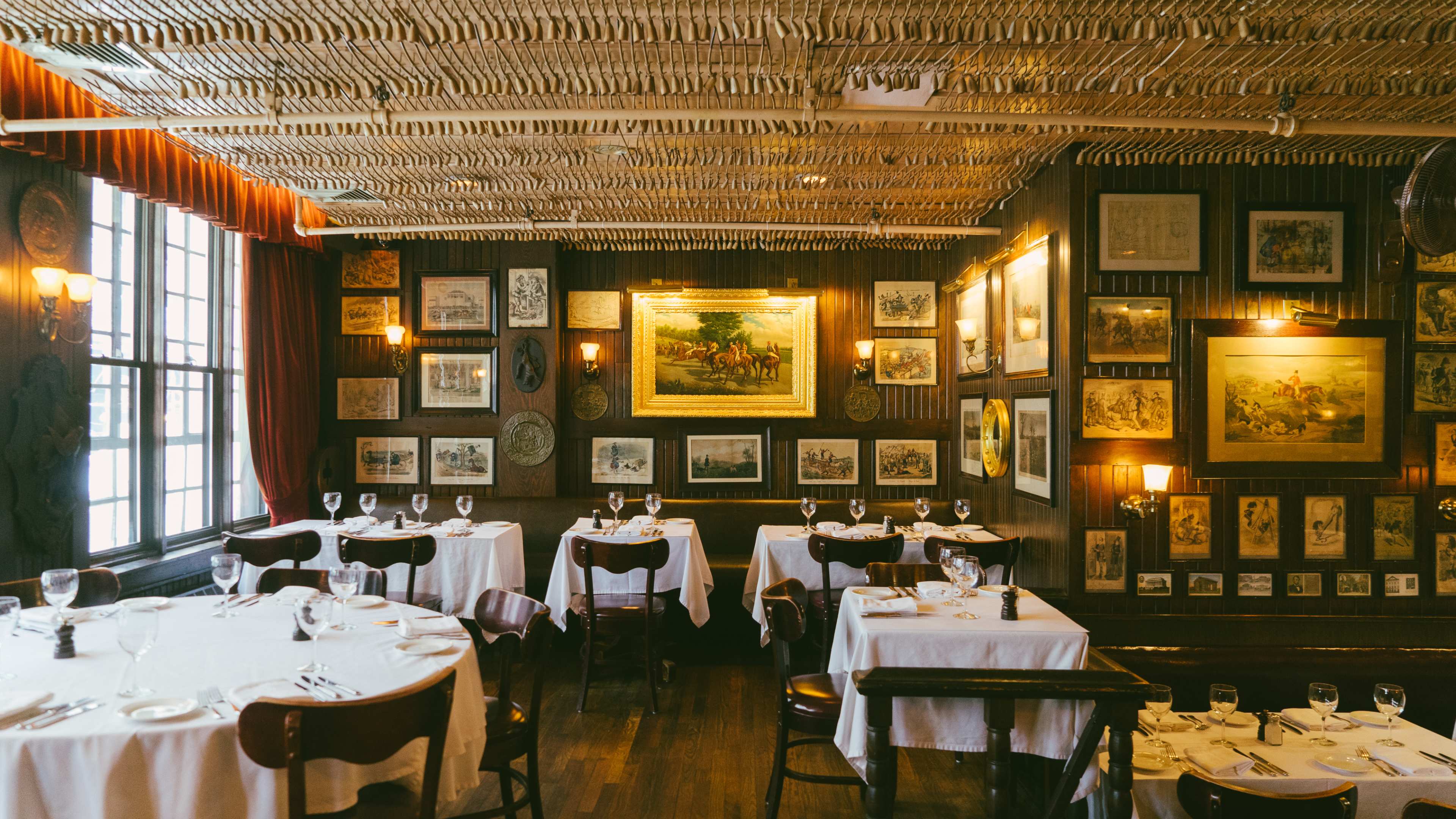 The itnerior of Keen's Steakhouse. There are framed photos covering the walls, tables with white tablecloths, and a textured pattern on the ceiling.