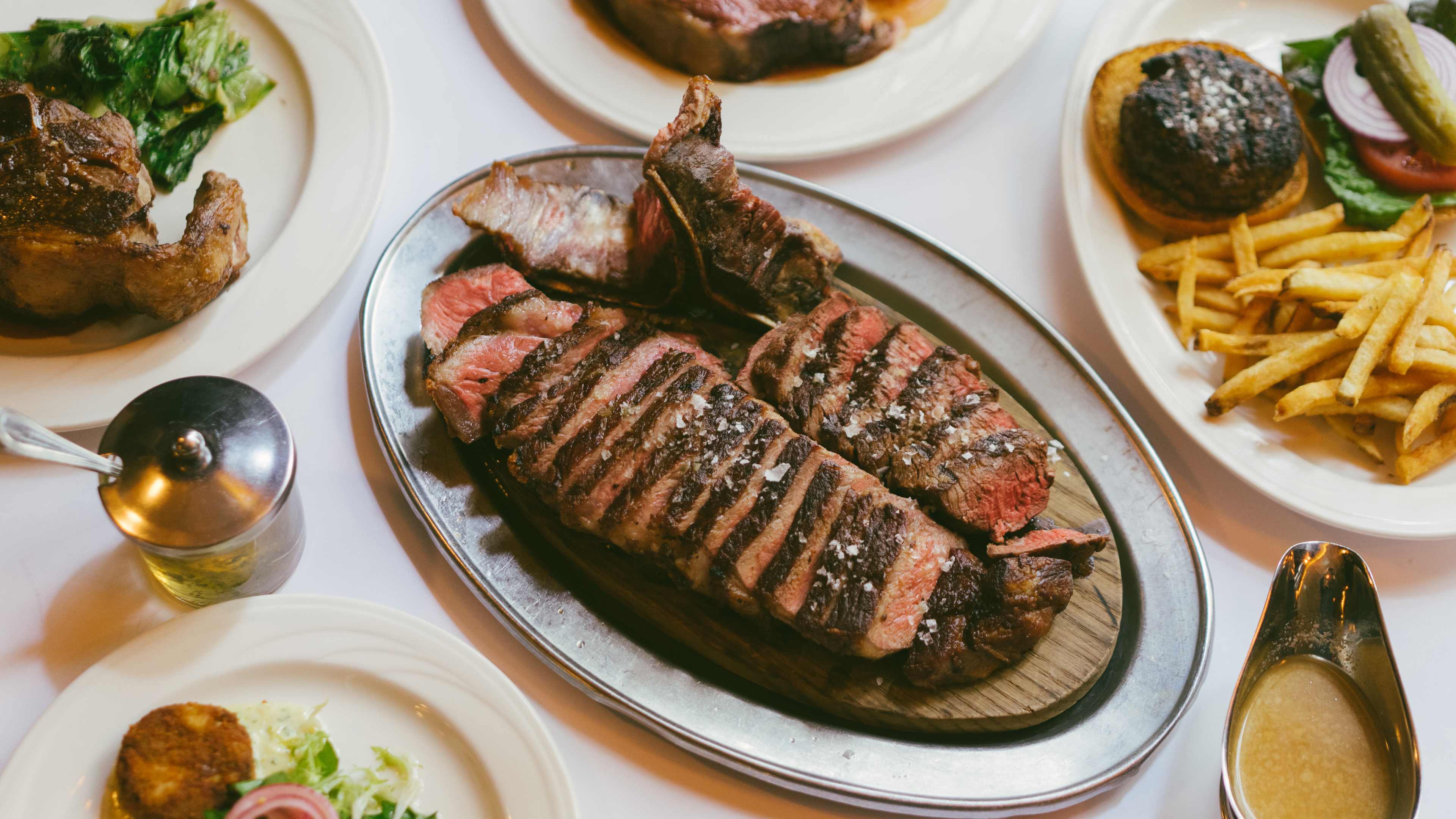 A spread of Keen's dishes. A steak is in the center, cut in pieces and garnished with salt.