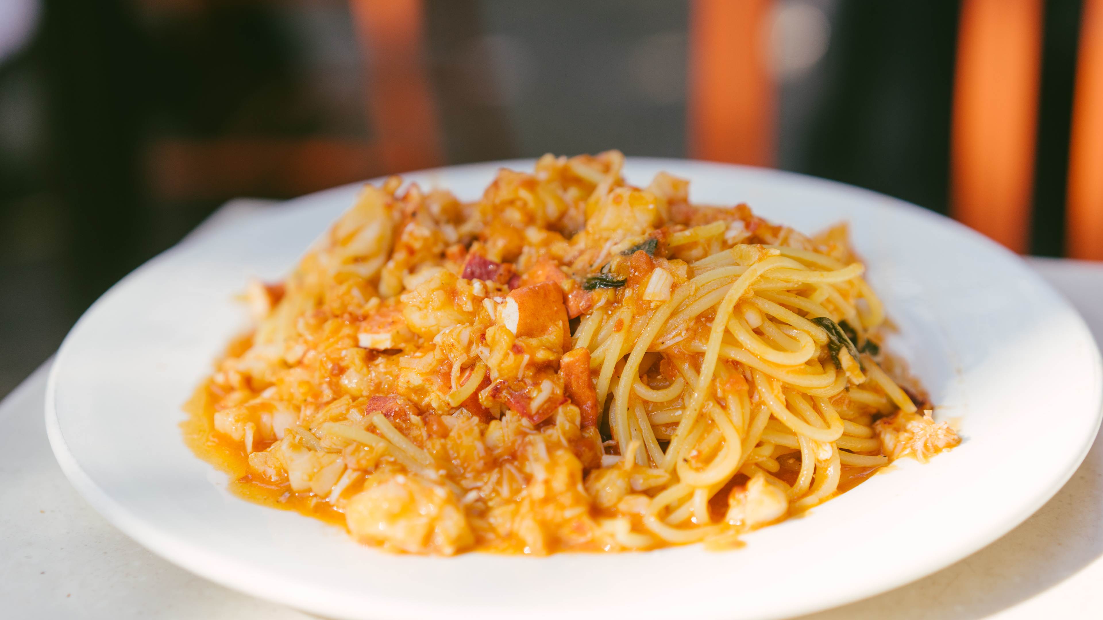 A plate of pasta topped with chunks of lobster in a sauce