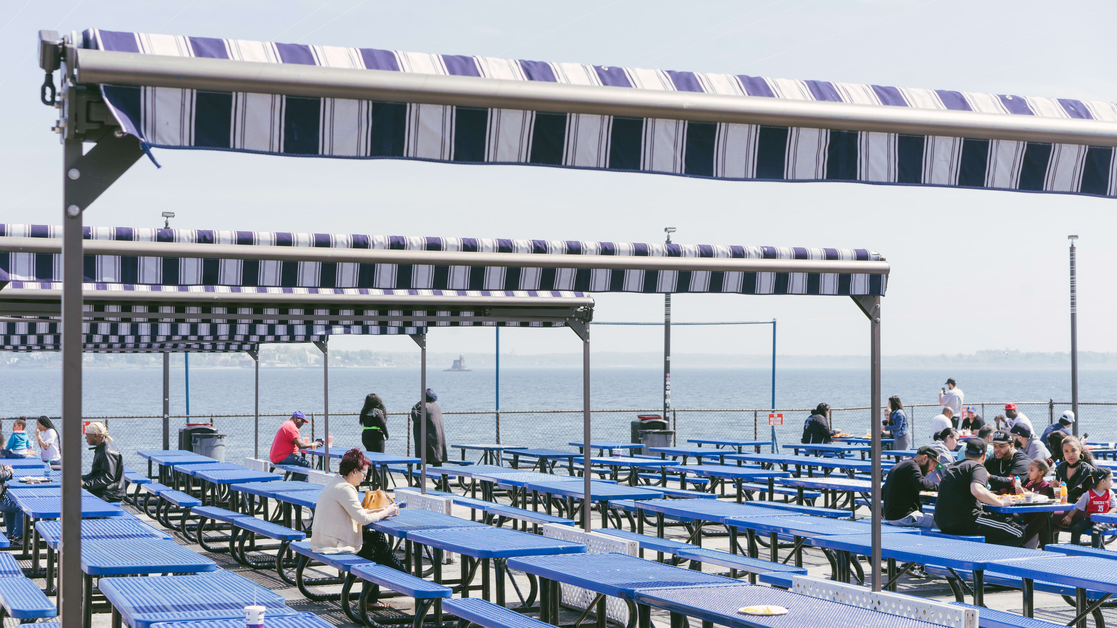 A patio covered in big blue picnic tables near the water on City Island.