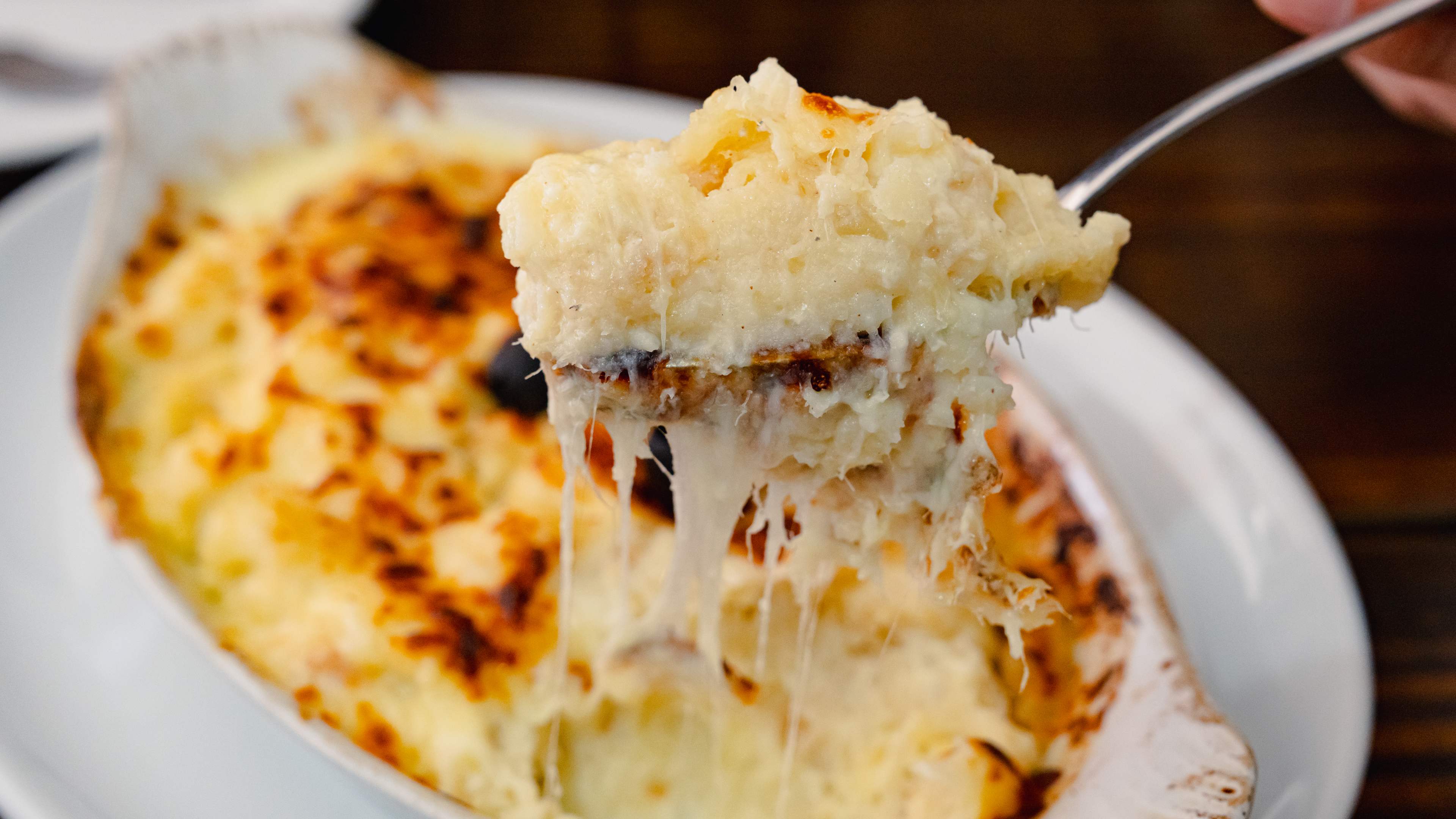 A spoon lifting up cheesy bacalhau com natas.