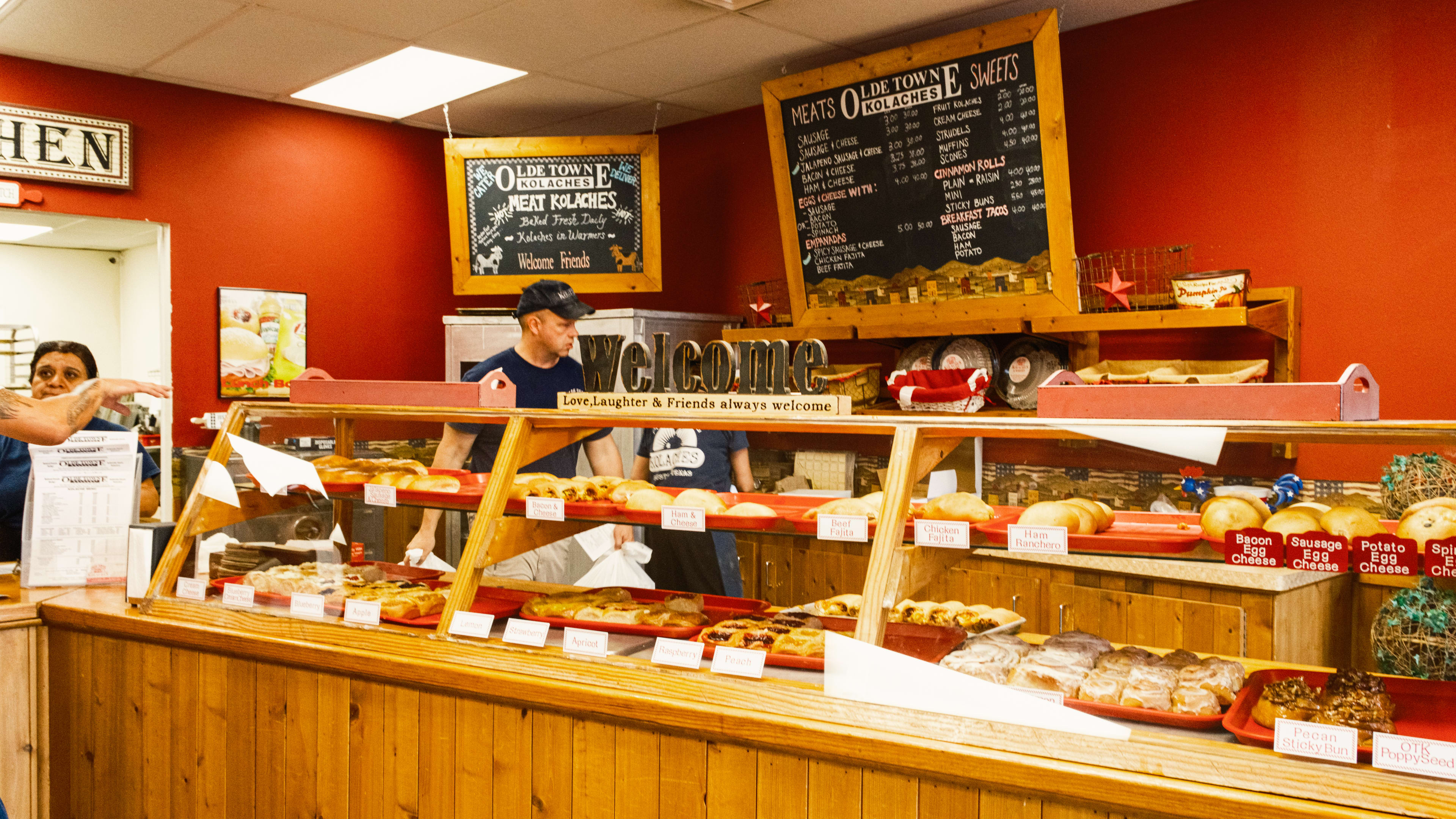 The wooden pastry case at Olde Towne Kolaches. The walls are red and there are red and white gingham accents.