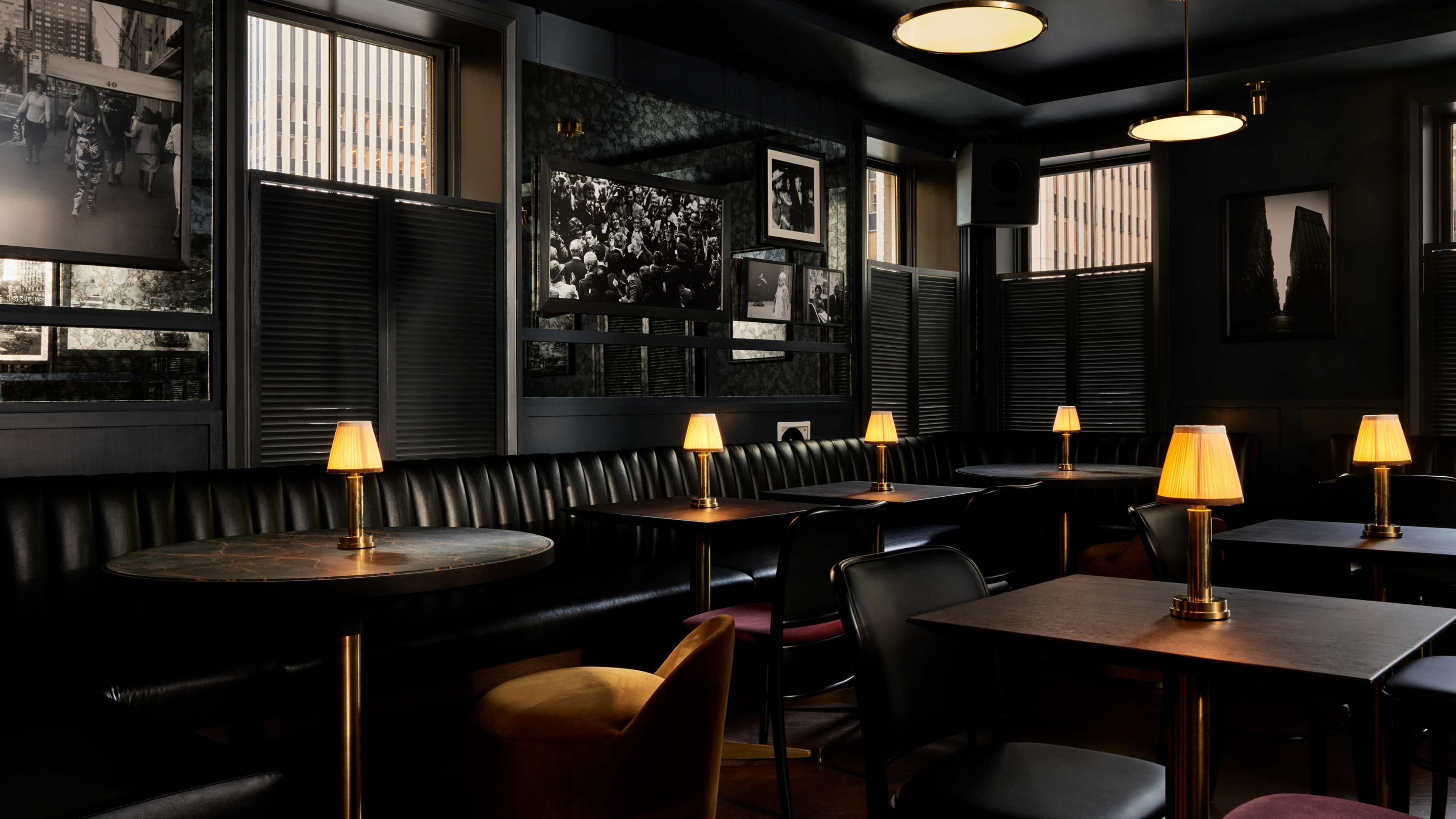 The dining area on the third floor at Pebble Bar lit by small lamps on each table. There are black leather booths and framed art on the walls.
