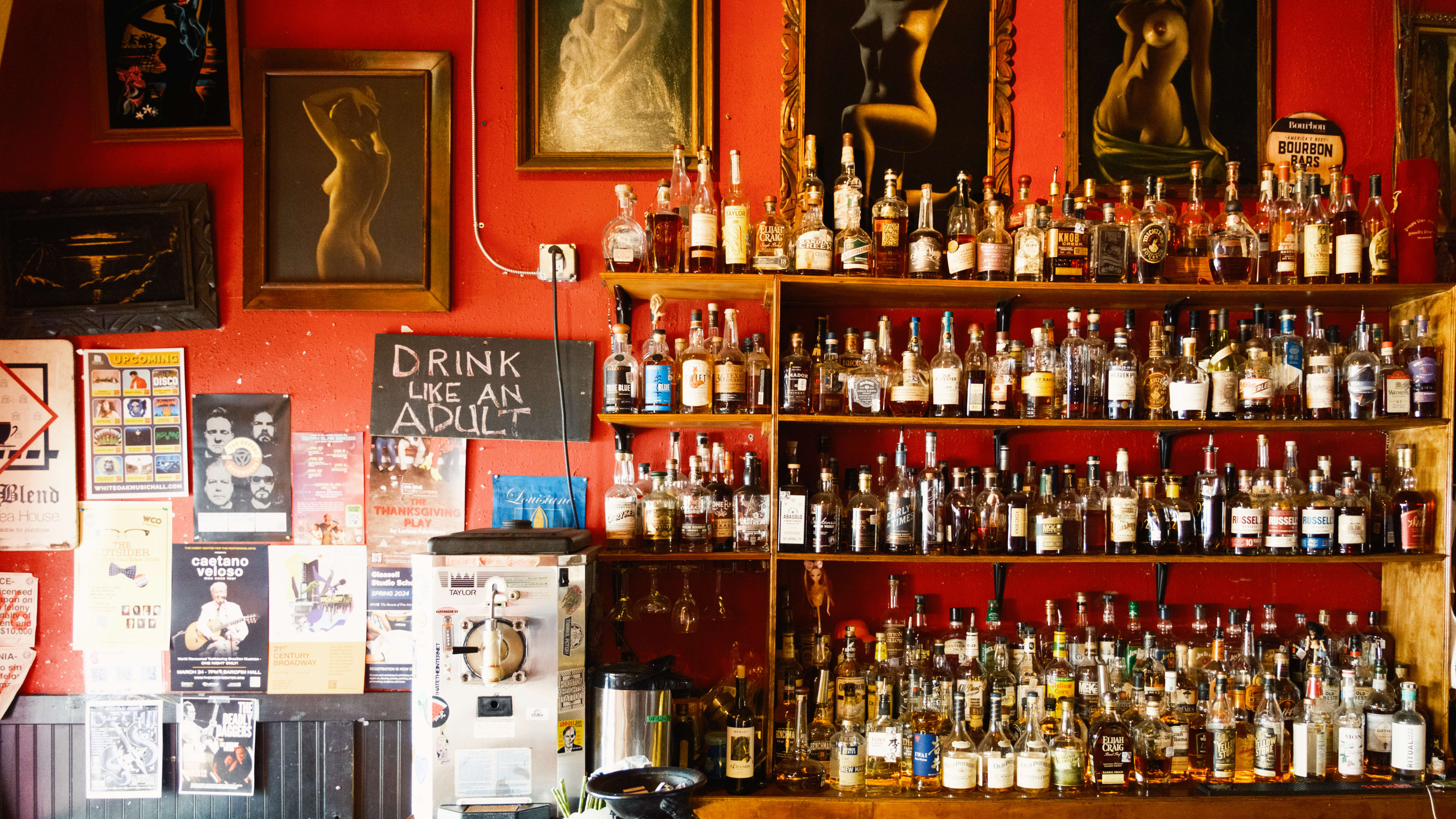 The bar at Poison Girl.  With framed nude paintings, a large whiskey selection, and posters on the red wall.