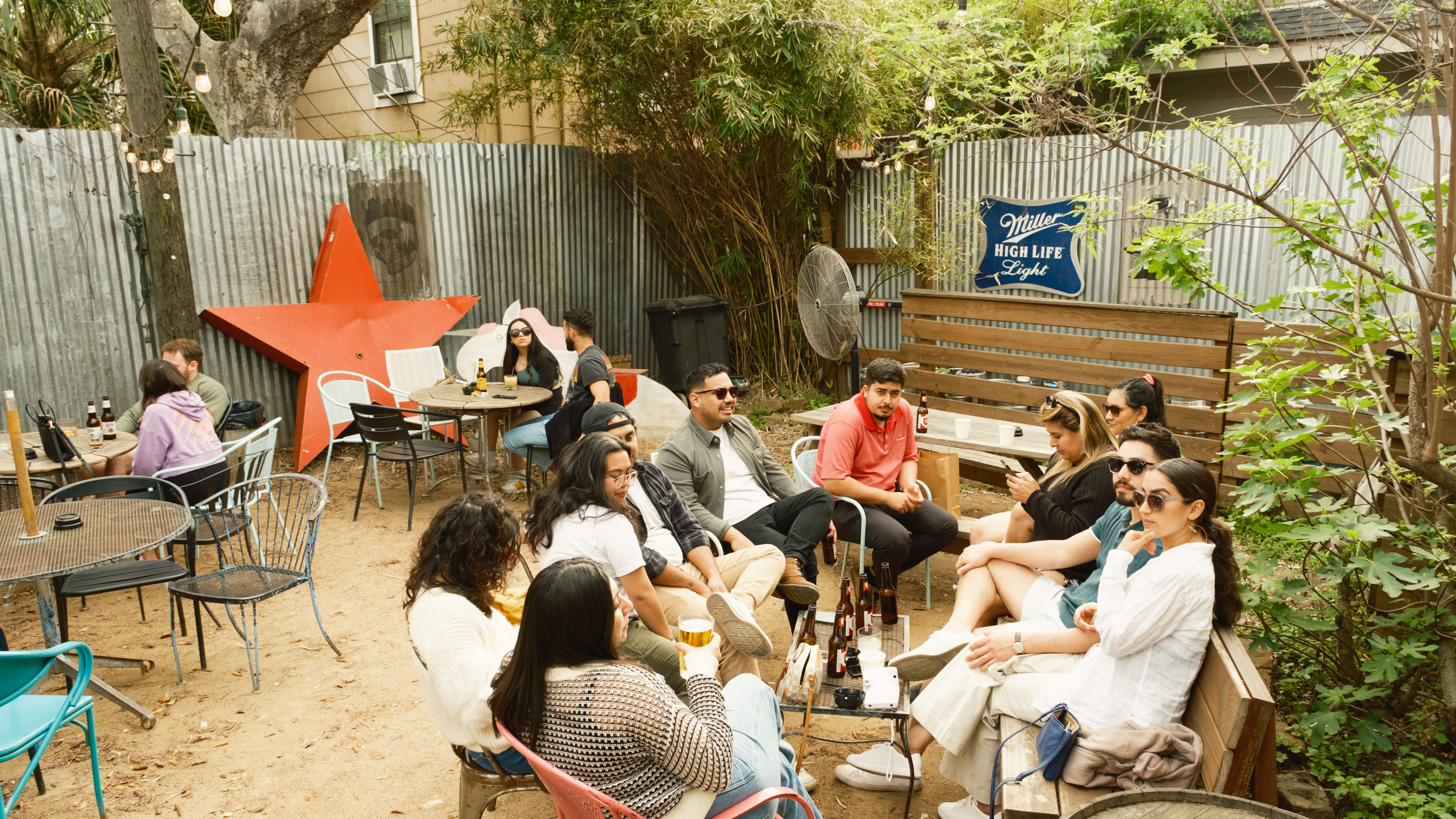 A group of people on the patio at Poison Girl. The ground is sand and there is a metal fence and hanging string lights.