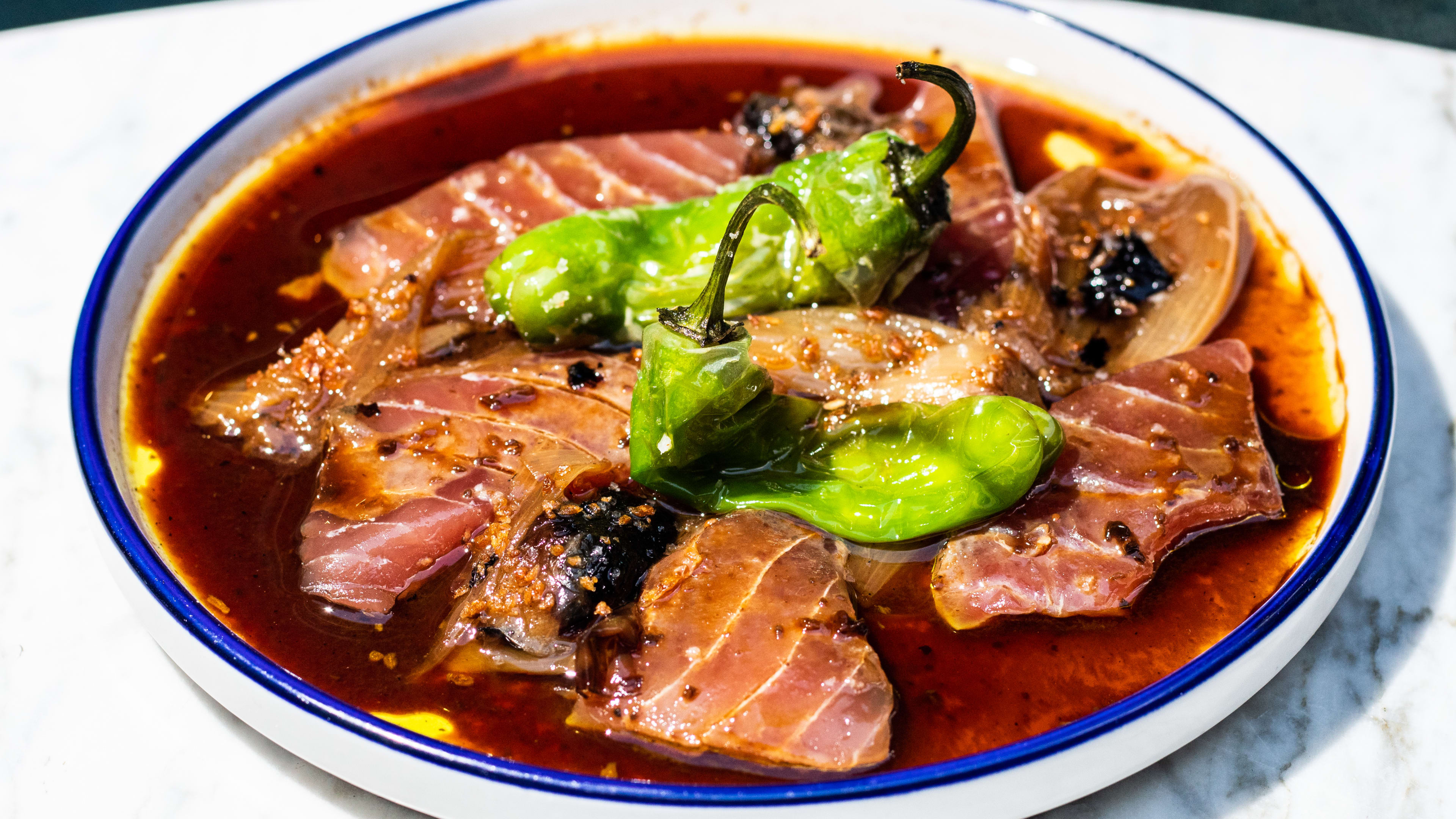 A plate of tuna crudo with peppers on top.