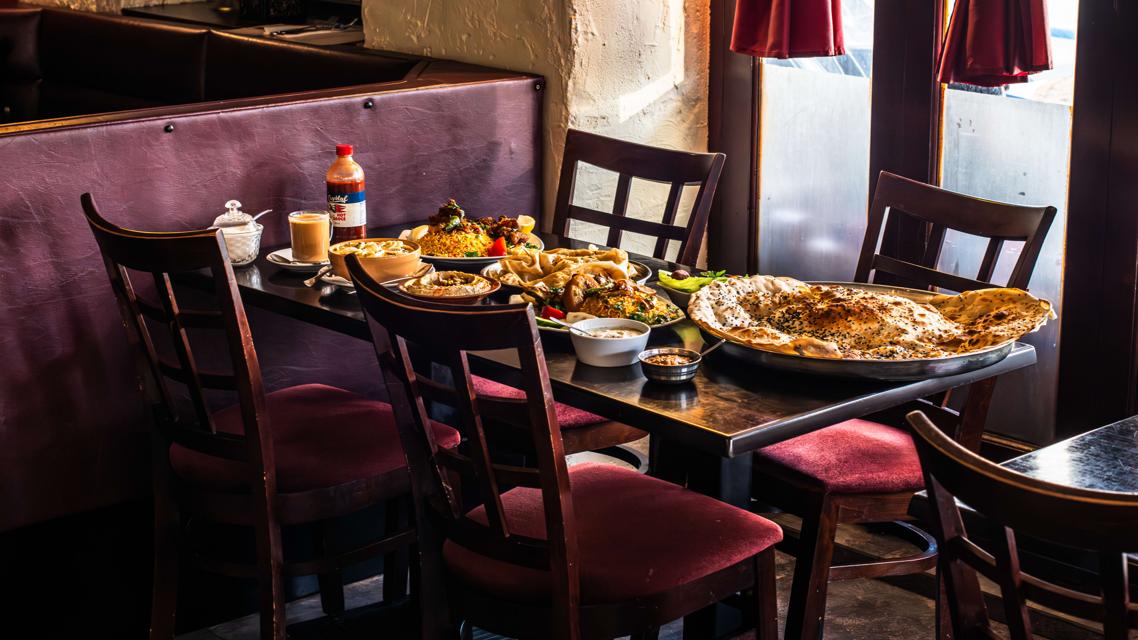 A spread of Yemeni food on a wooden table with four wooden chairs with red cushions.