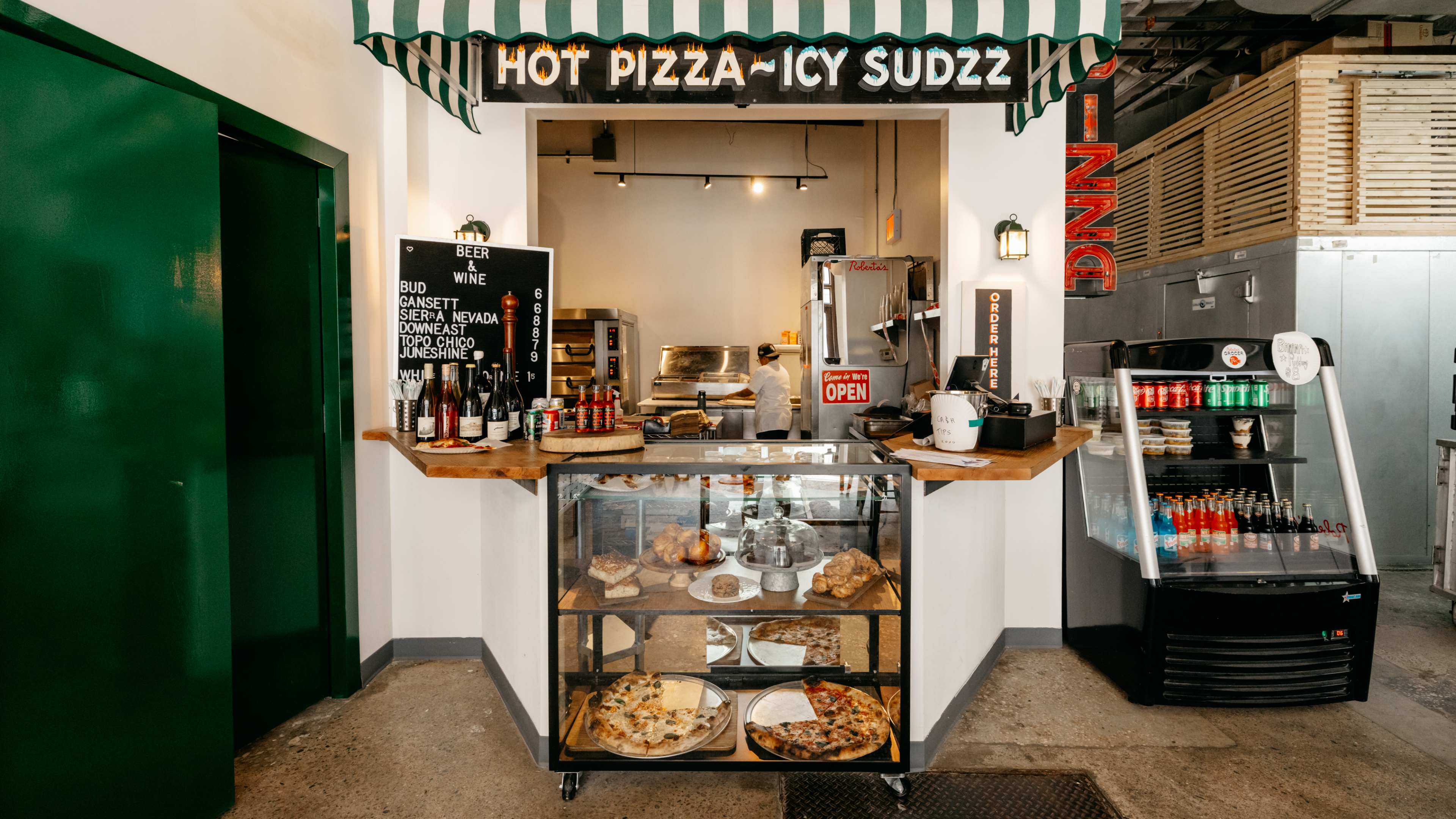 A counter with a green awning and a glass case with baked goods inside R Slice pizza.
