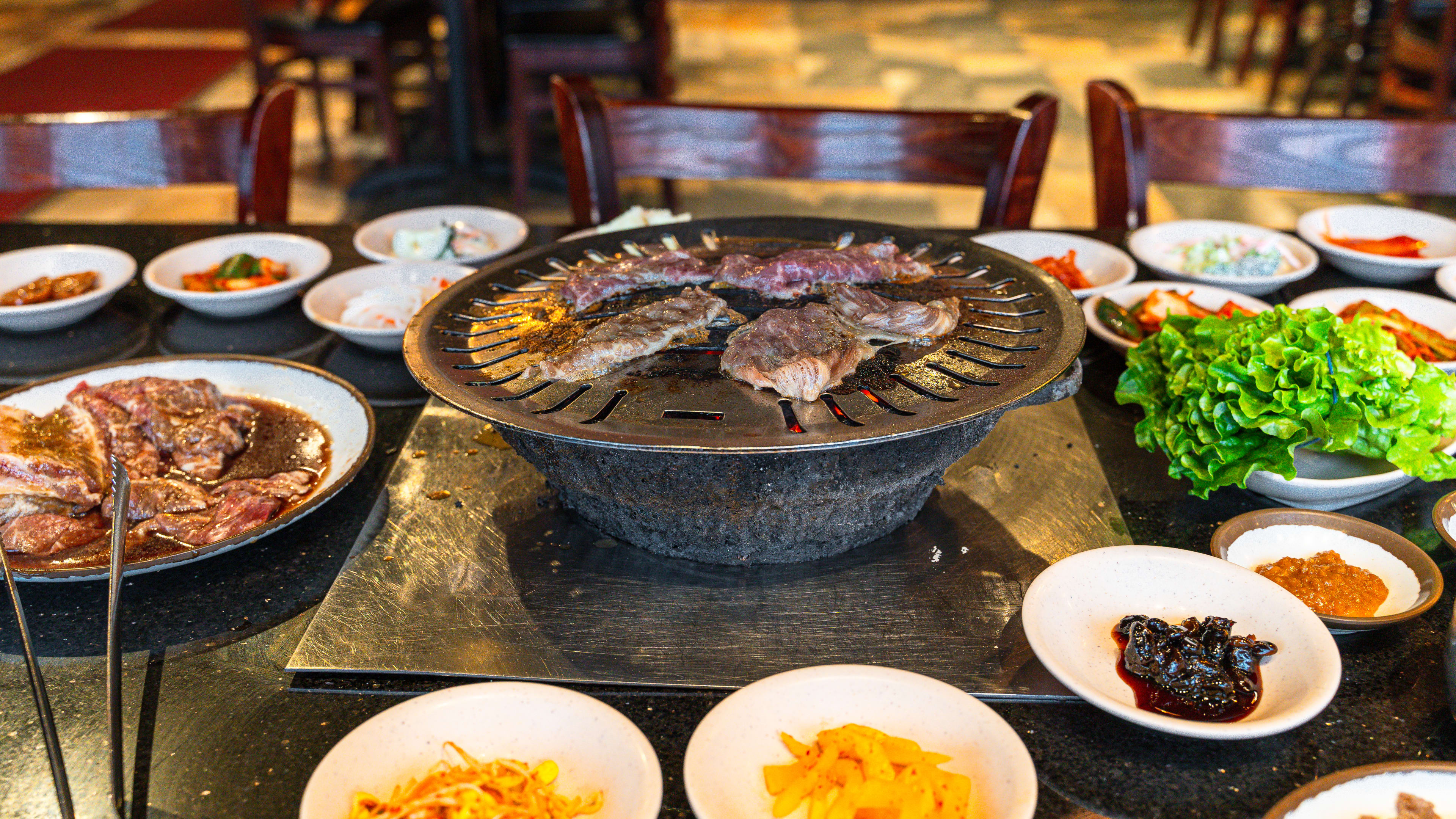 Kalbi grilling on a charcoal grill, surrounded by many plates of banchan.