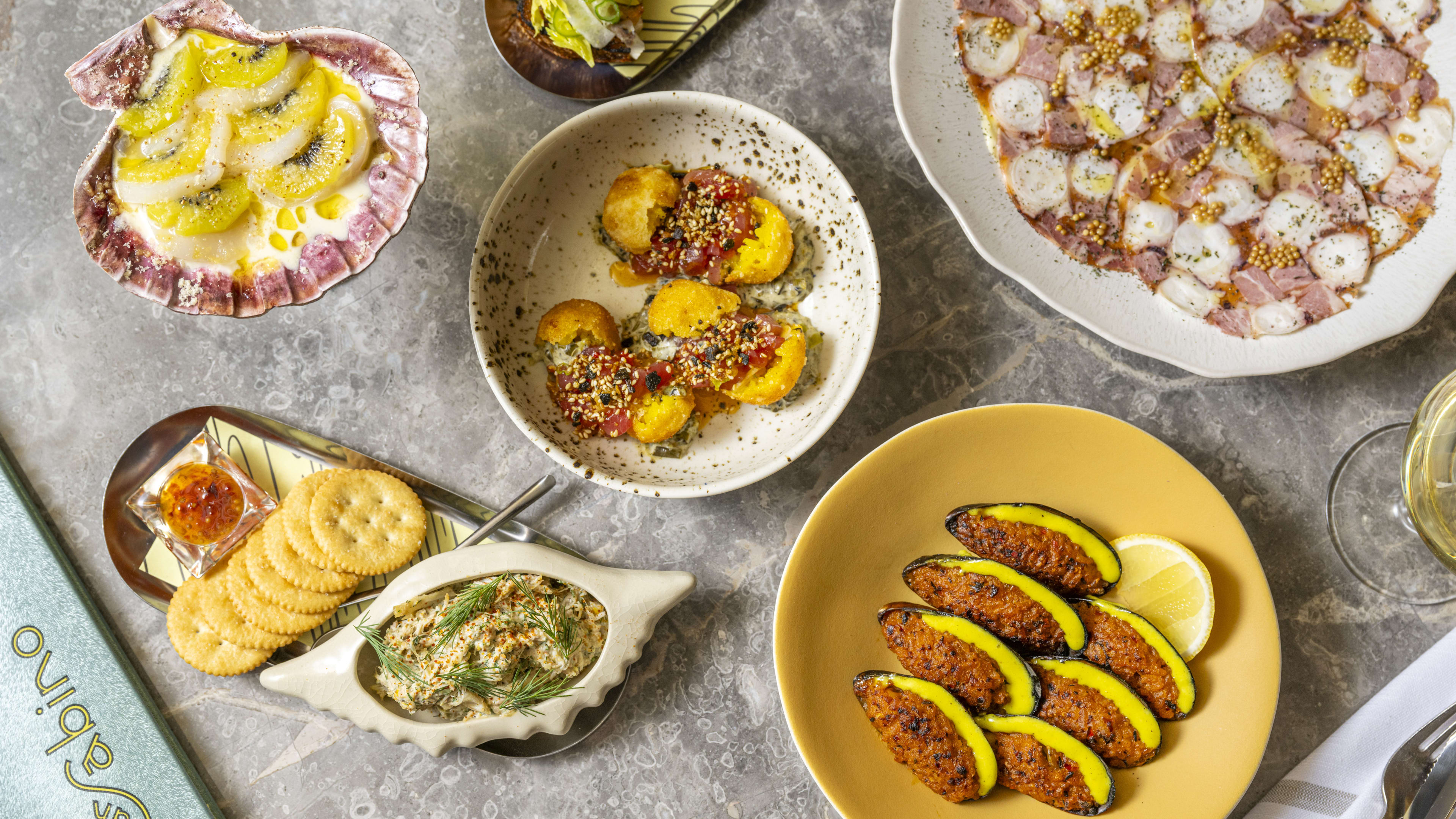 An array of seafood small plates arranged on a marble table.