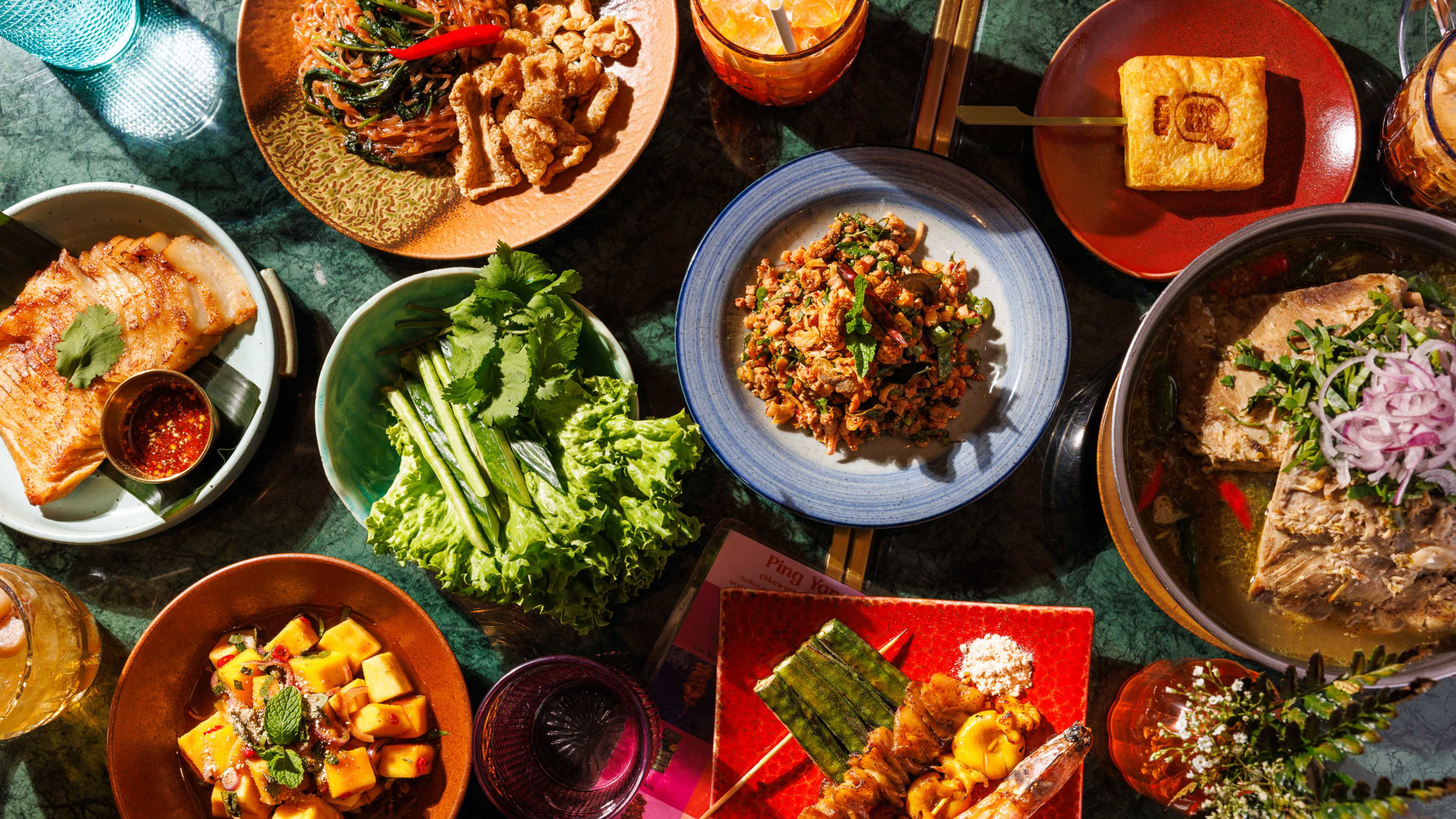 a spread of thai dishes from sappe, including some grilled skewers, a curry, a laab, and a noodle dish