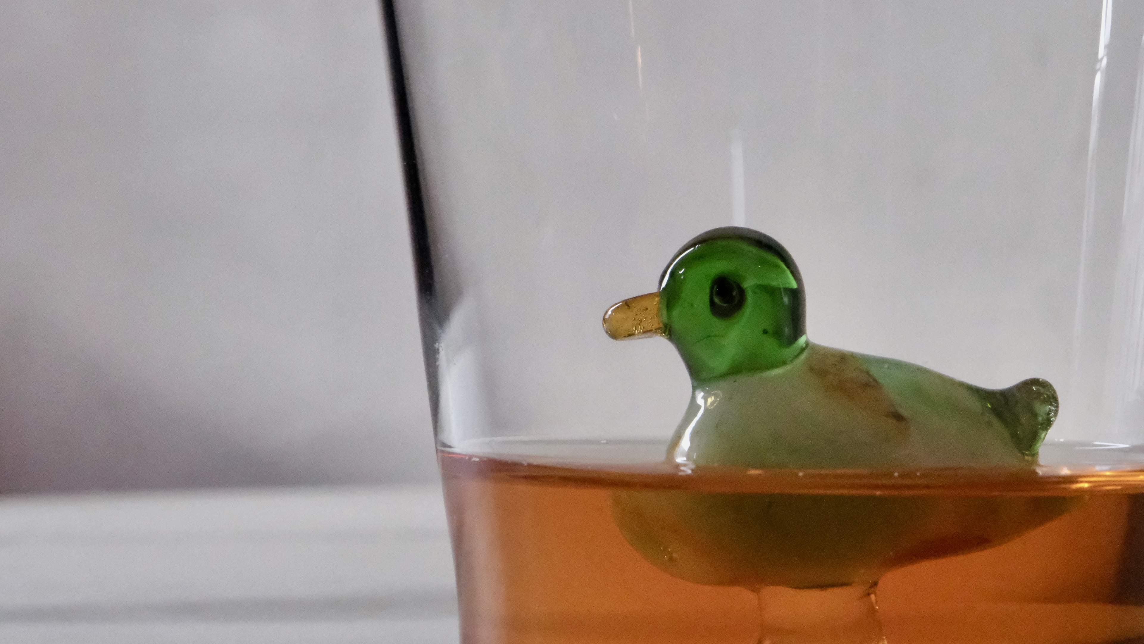 A cocktail served in a glass tumbler, with a glass duck inside the glass.