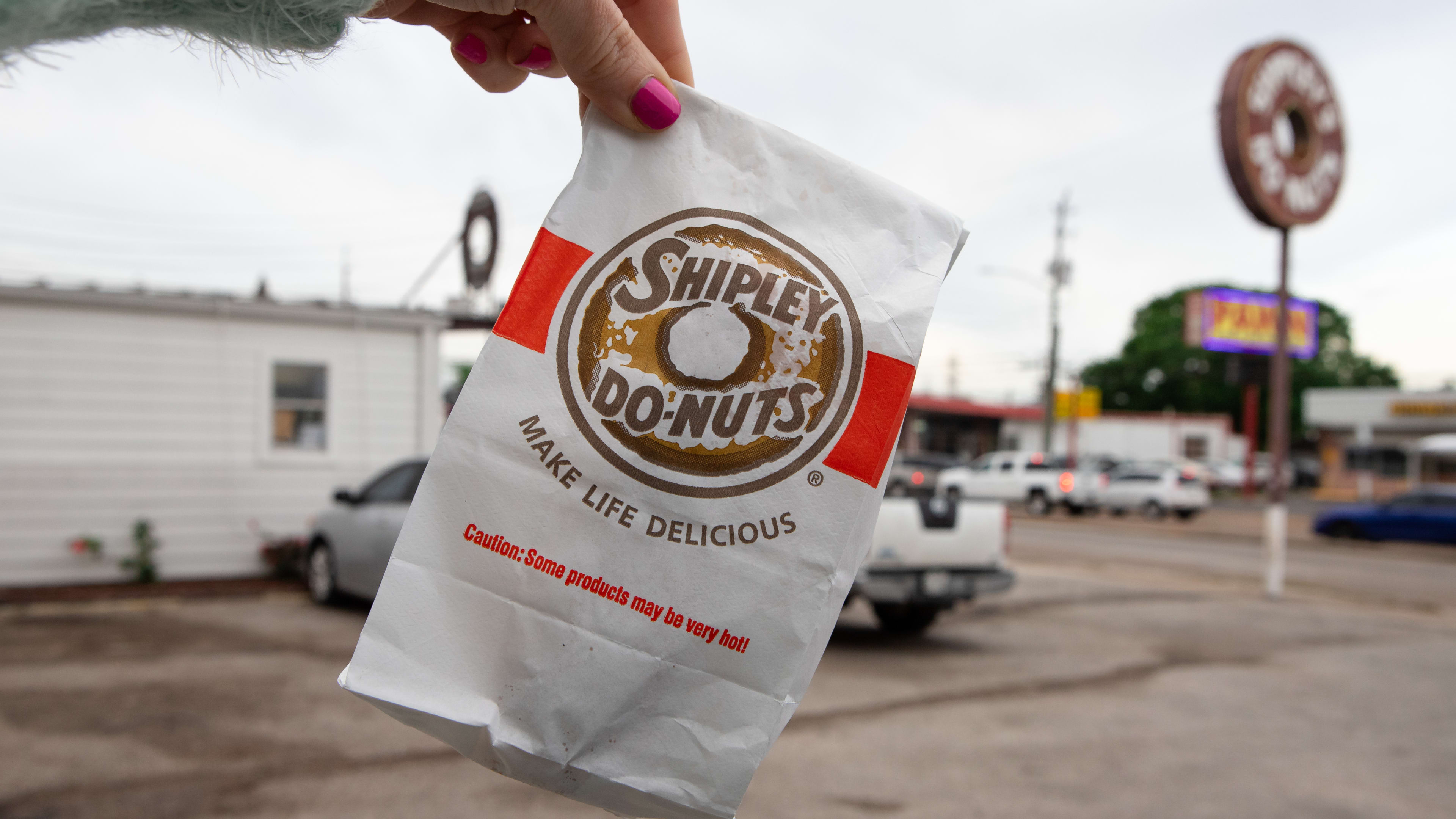 A person holds up a white Shipley's Do-Nuts bag.