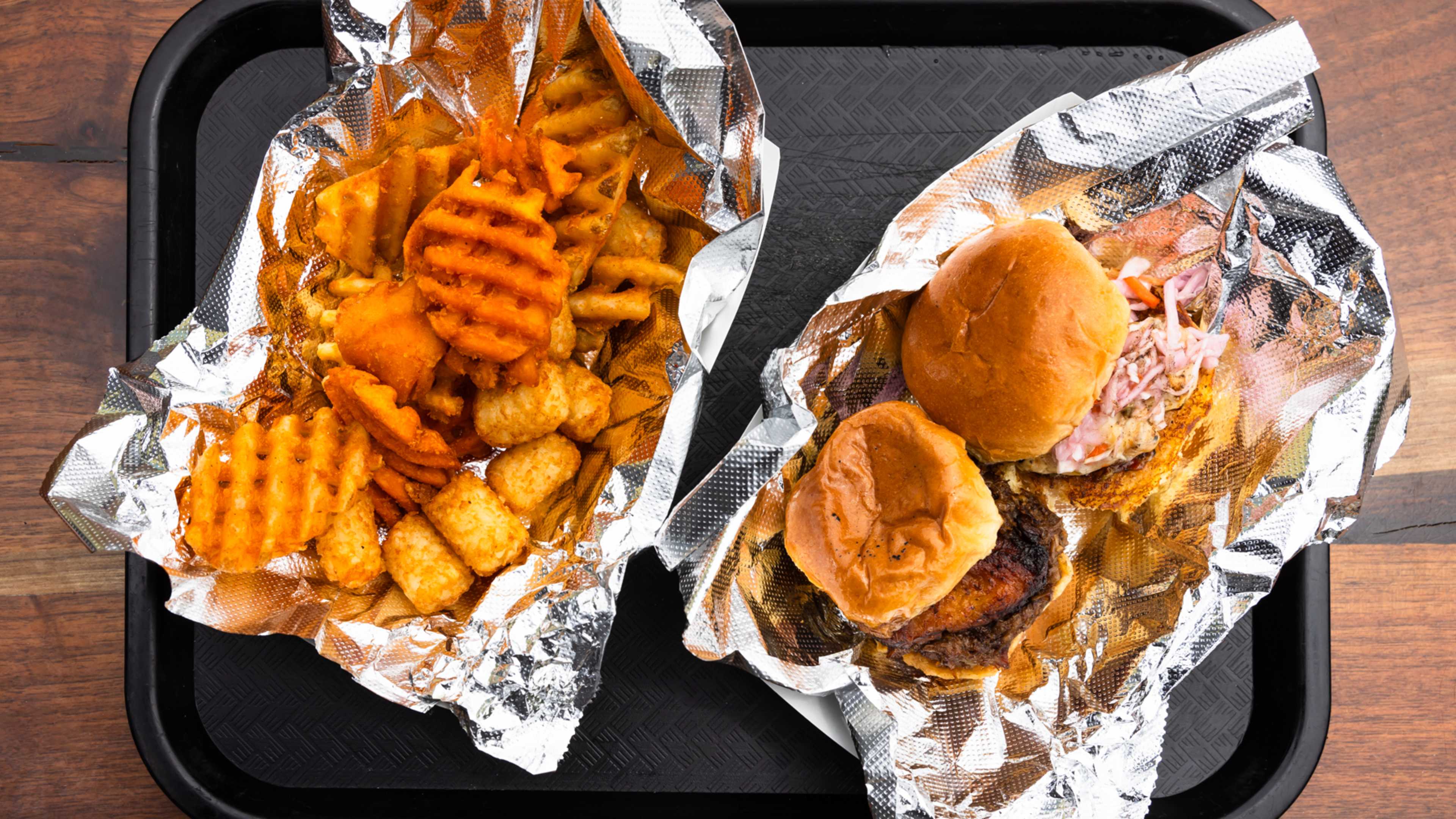 Two sliders and an assortment of french fries and tater tots on a black tray.