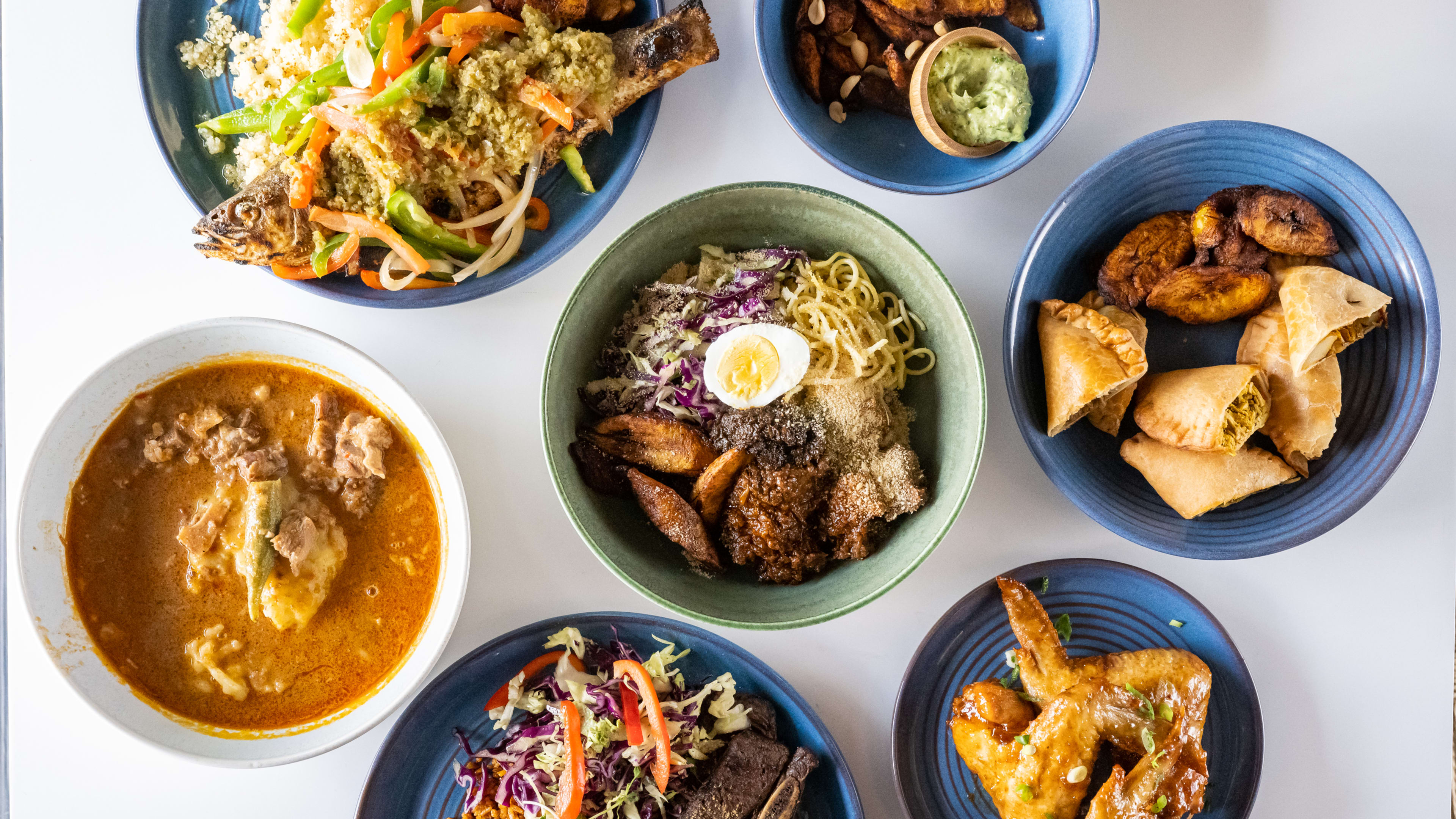 Spread of West African dishes, including chicken wings, handpies, fried fish, and fufu