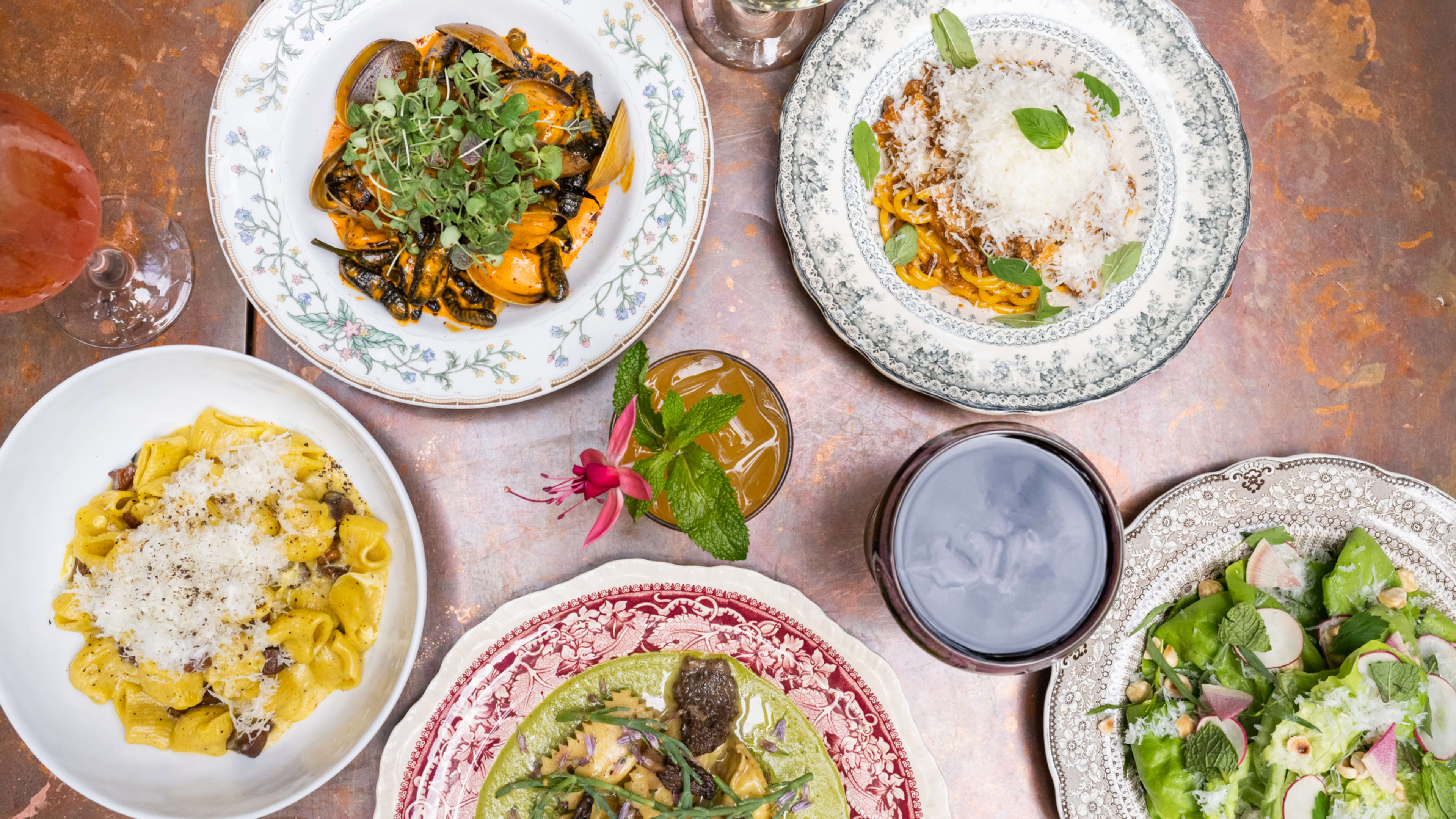 Spread of pasta, cocktails, wine, and salad on a brushed bronze table