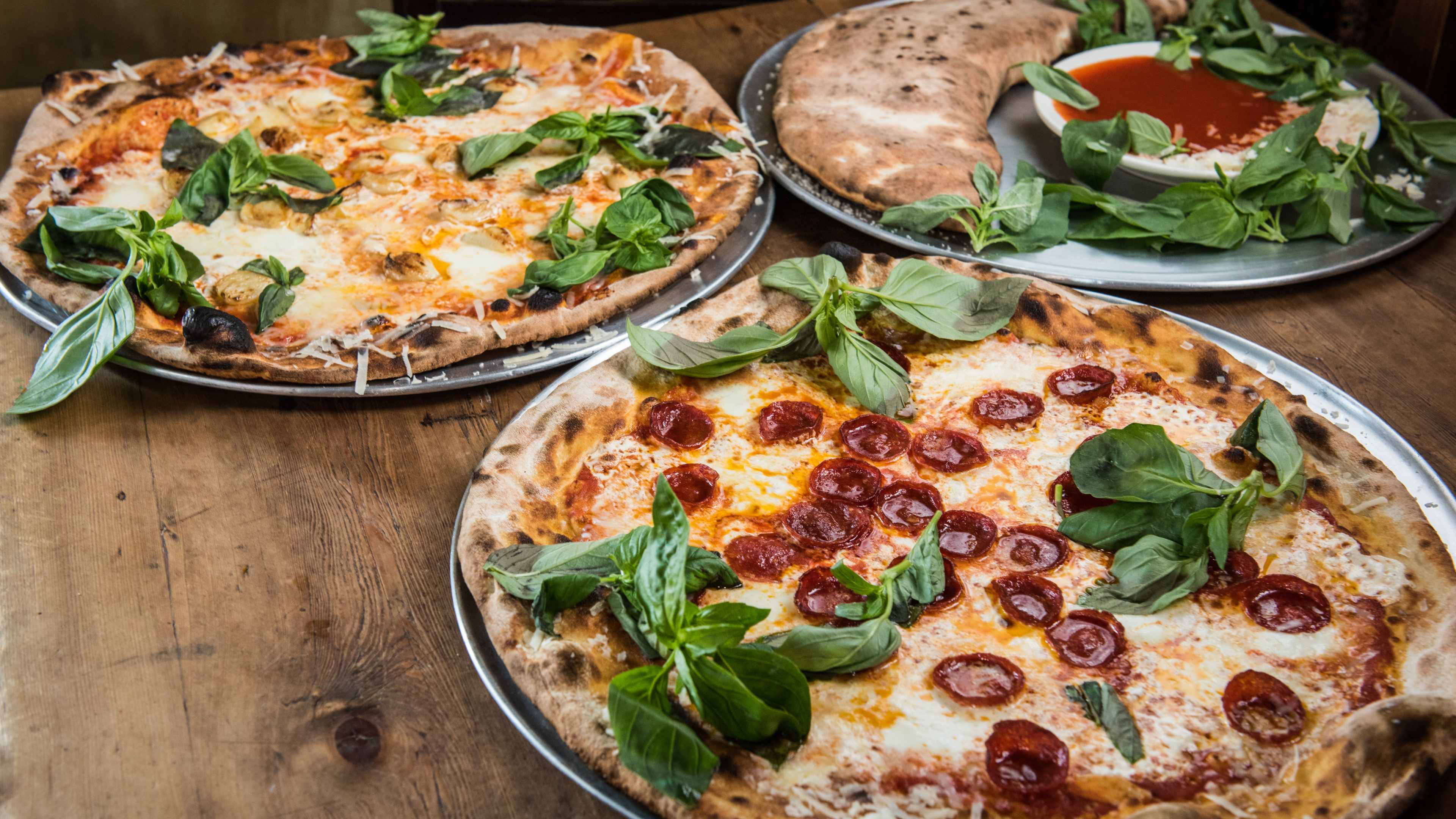 Three different kinds of pizza from Lucali on a wooden surface.