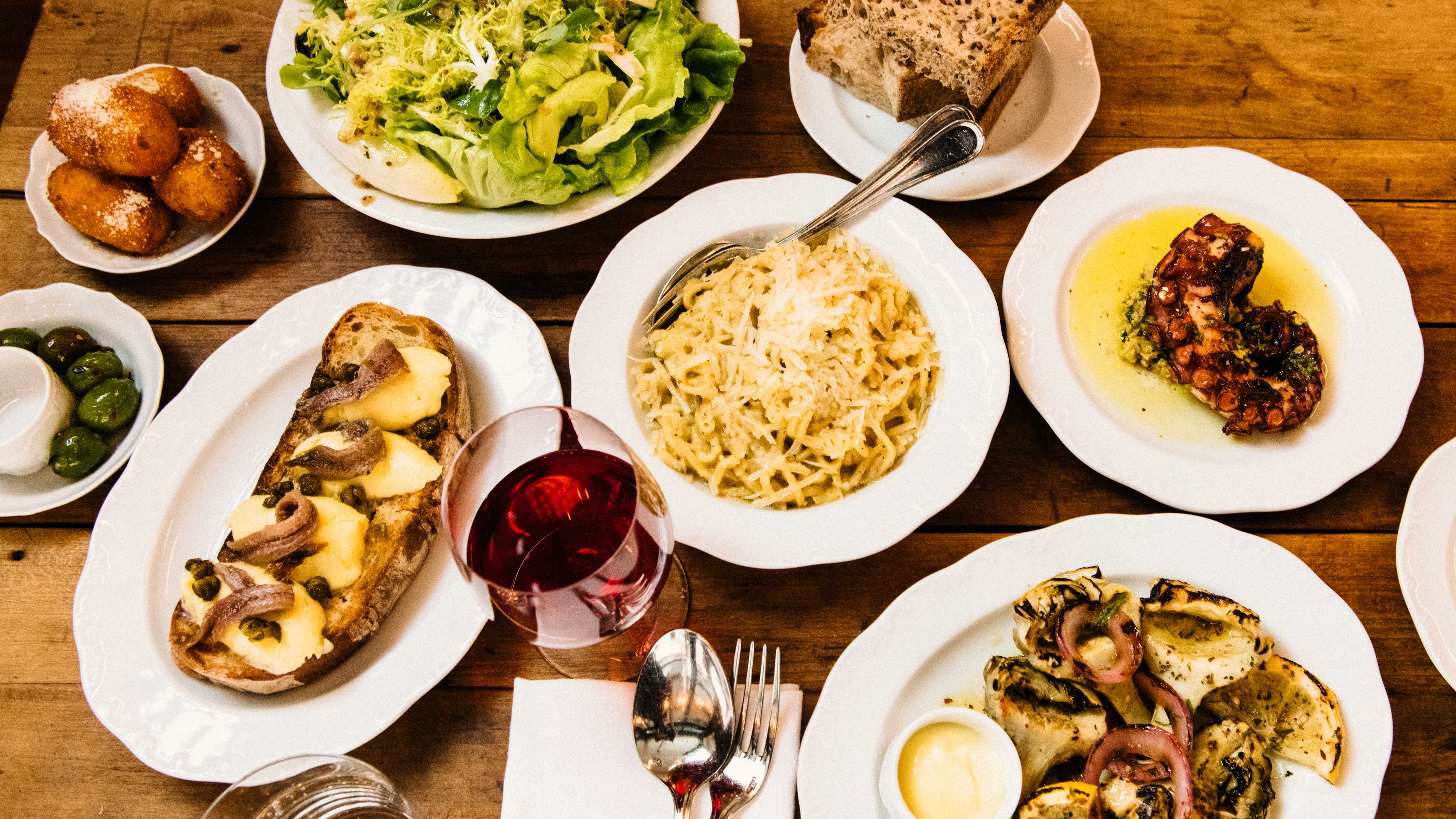 A spread of dishes and a glass of wine from Via Carota on a wooden table