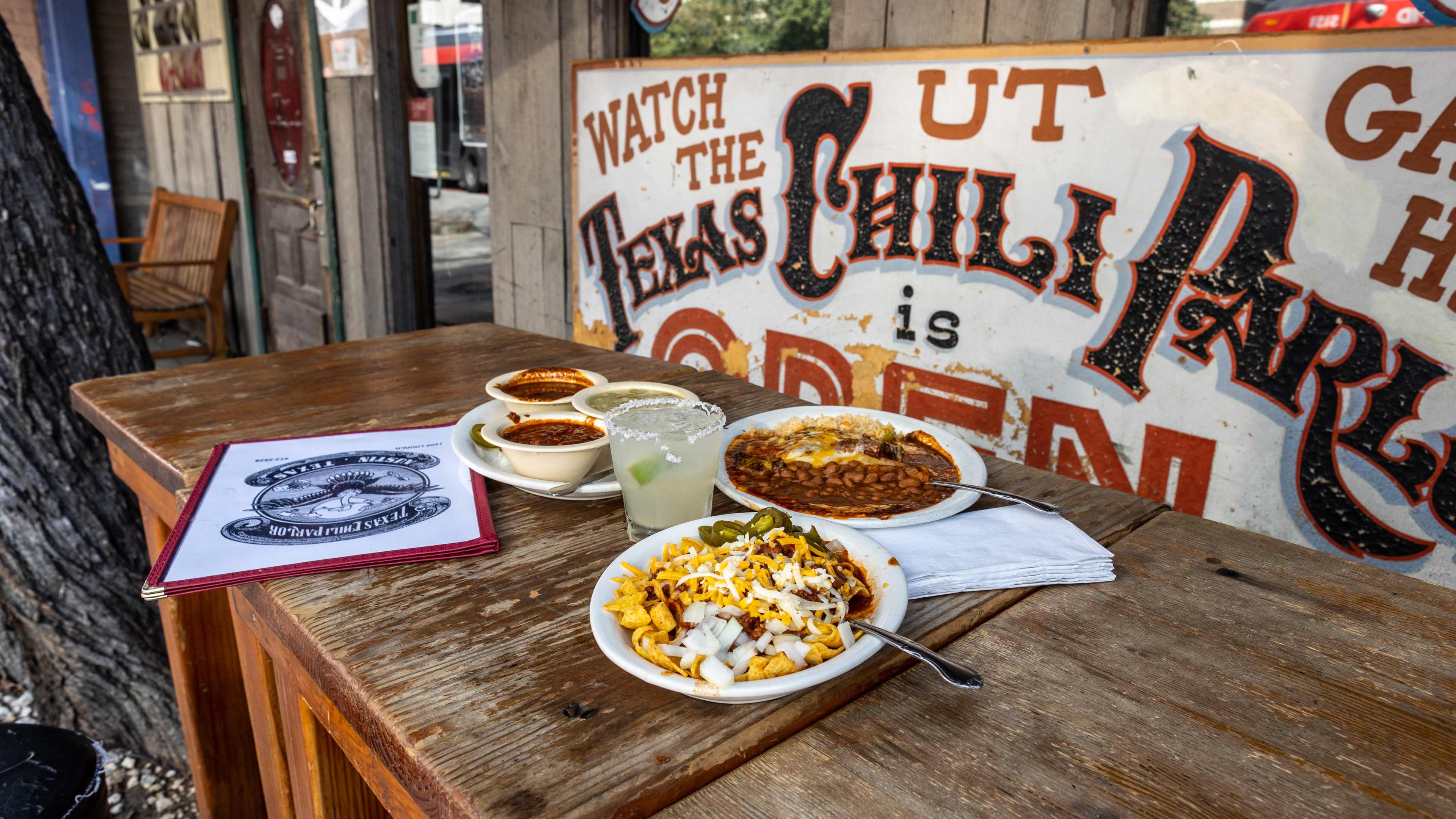 A group of dishes sitting on a wooden table on the patio at Texas Chili Parlor.