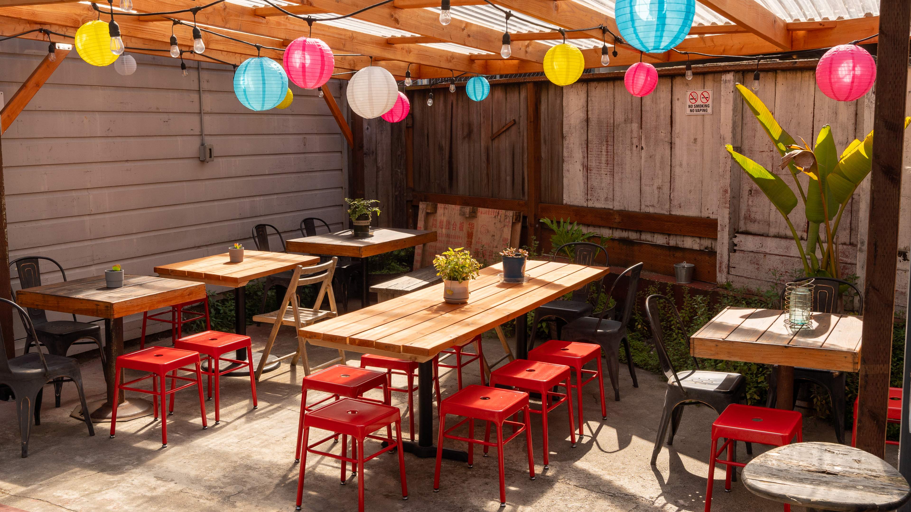 A back patio with wooden tables, red stool, and decorative lamps.