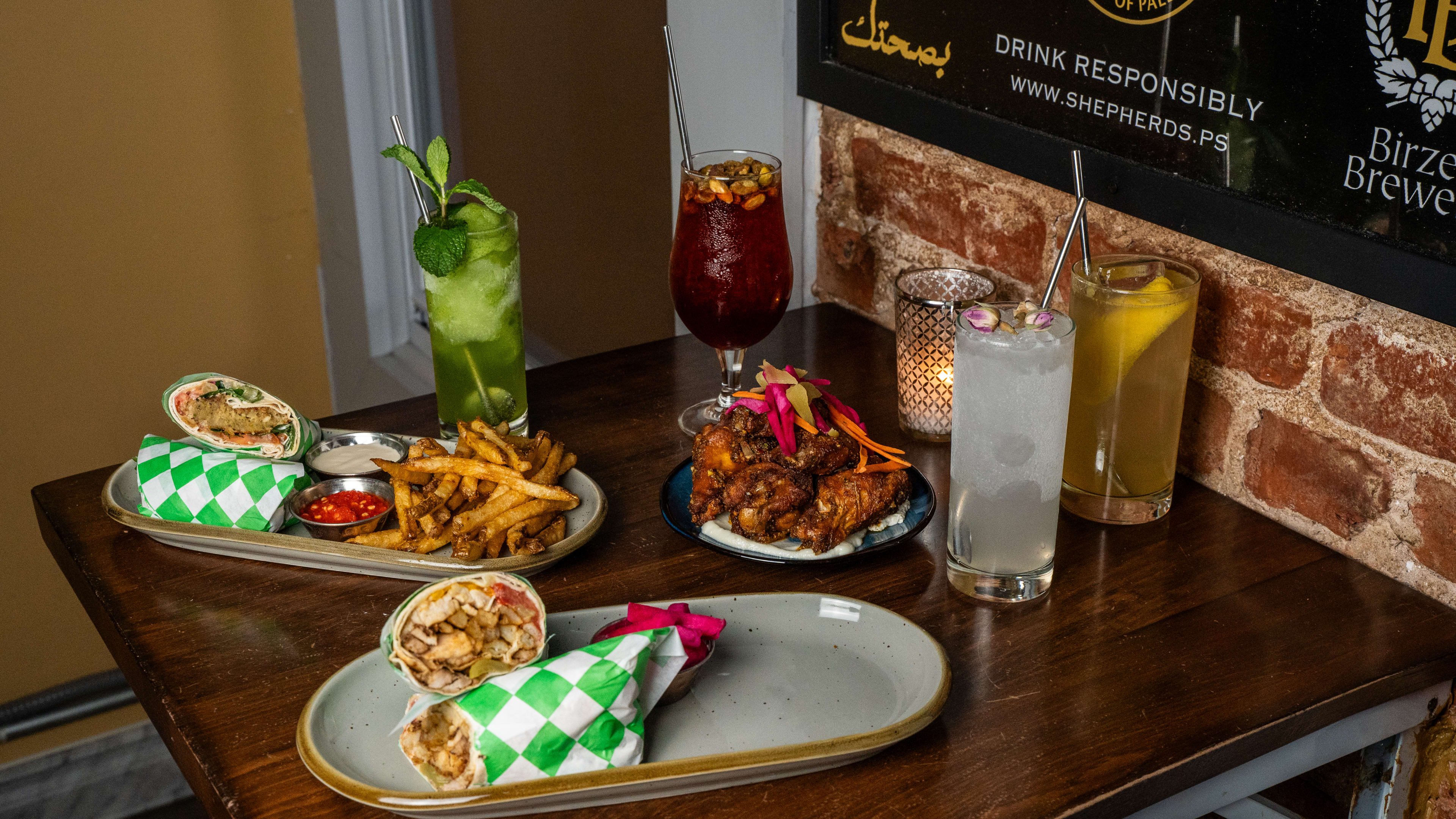 Spread of wraps, wings, fries, and cocktails on wooden table.