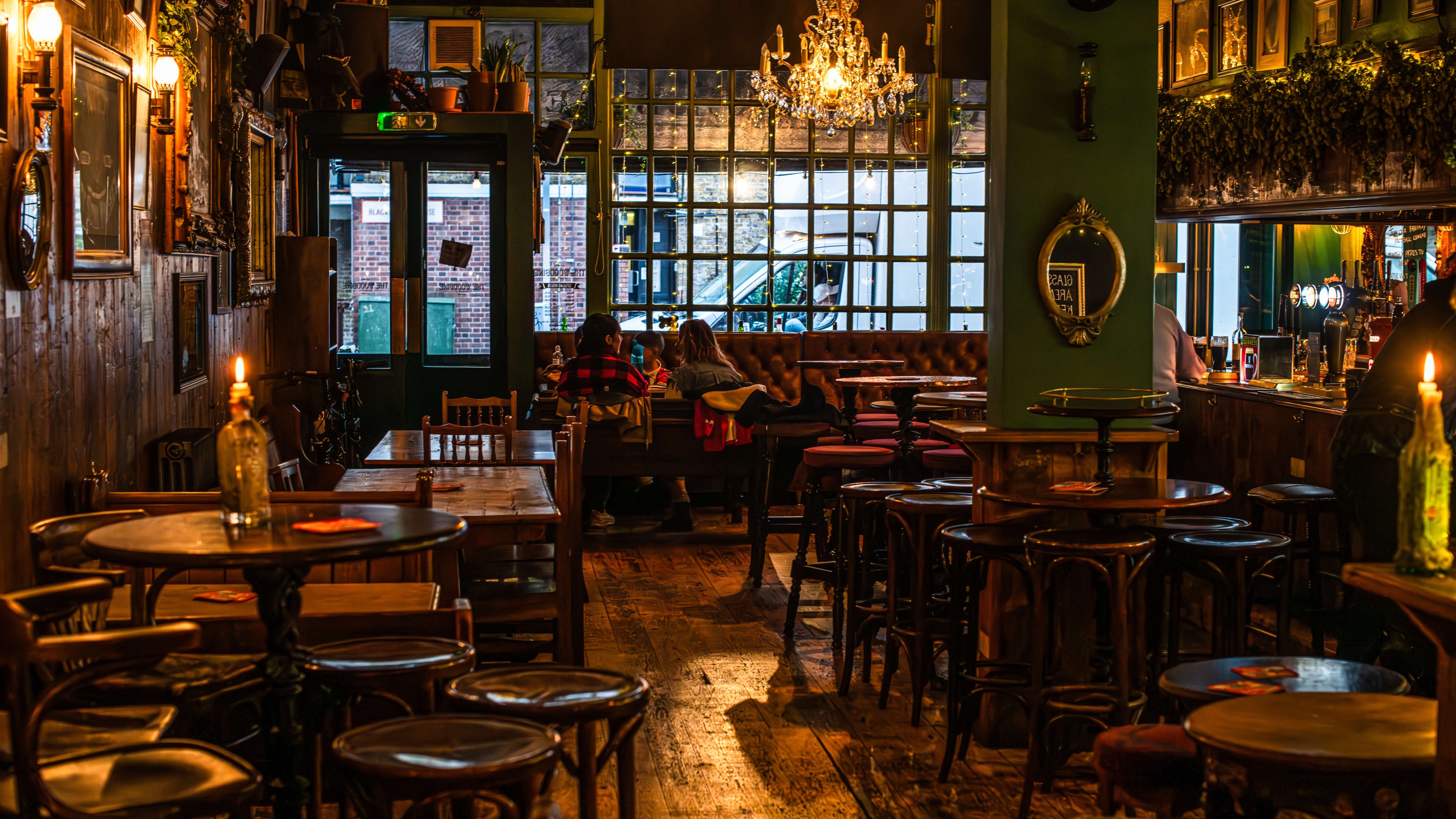 The dark, candle-lit interior of The Woodbine pub, with greenery hanging on the ceiling, framed photos and mirrors on the walls, a large chandelier and wooden tables