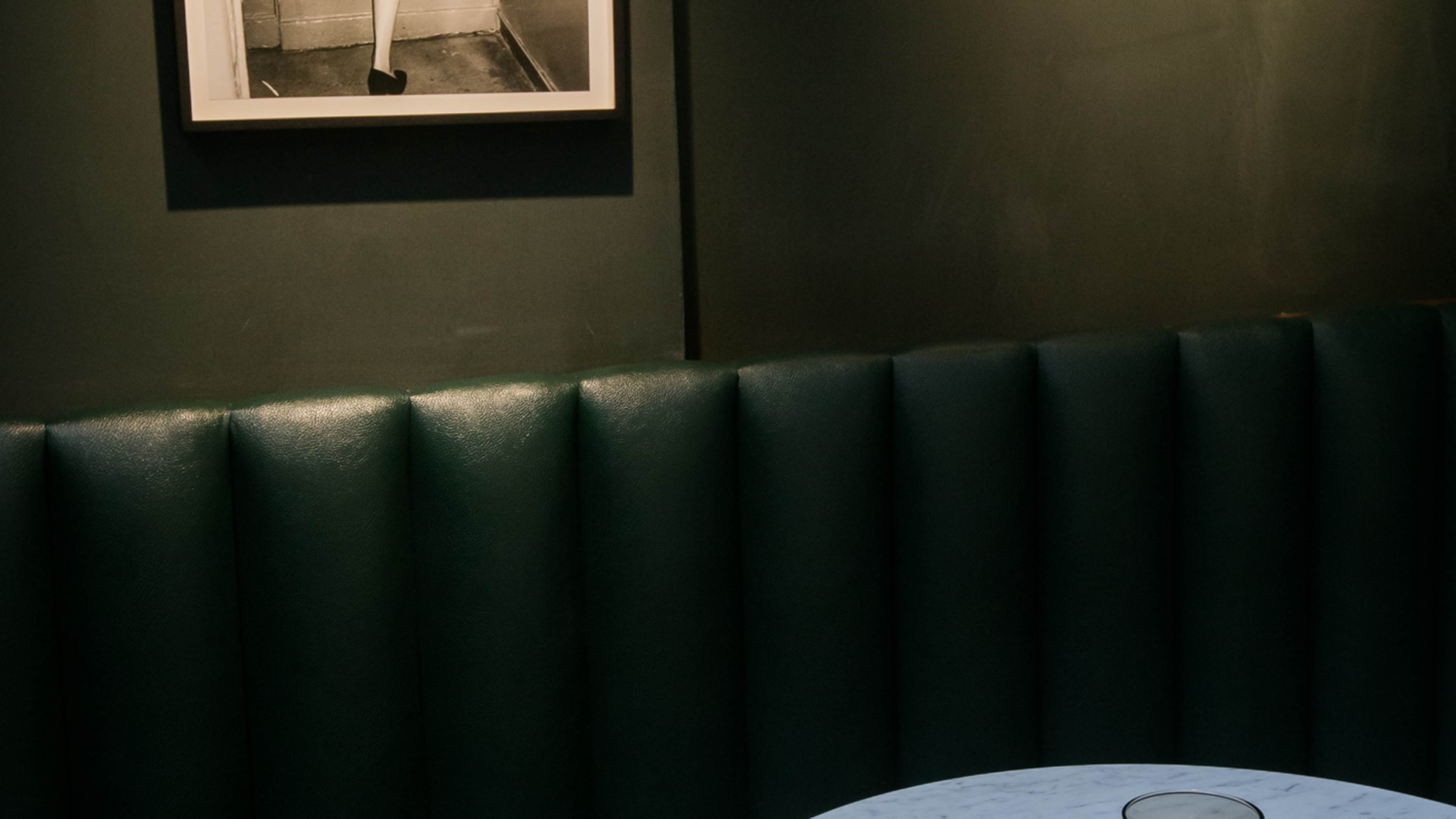 A moody green booth, with a marble-look table with a flickering candle.