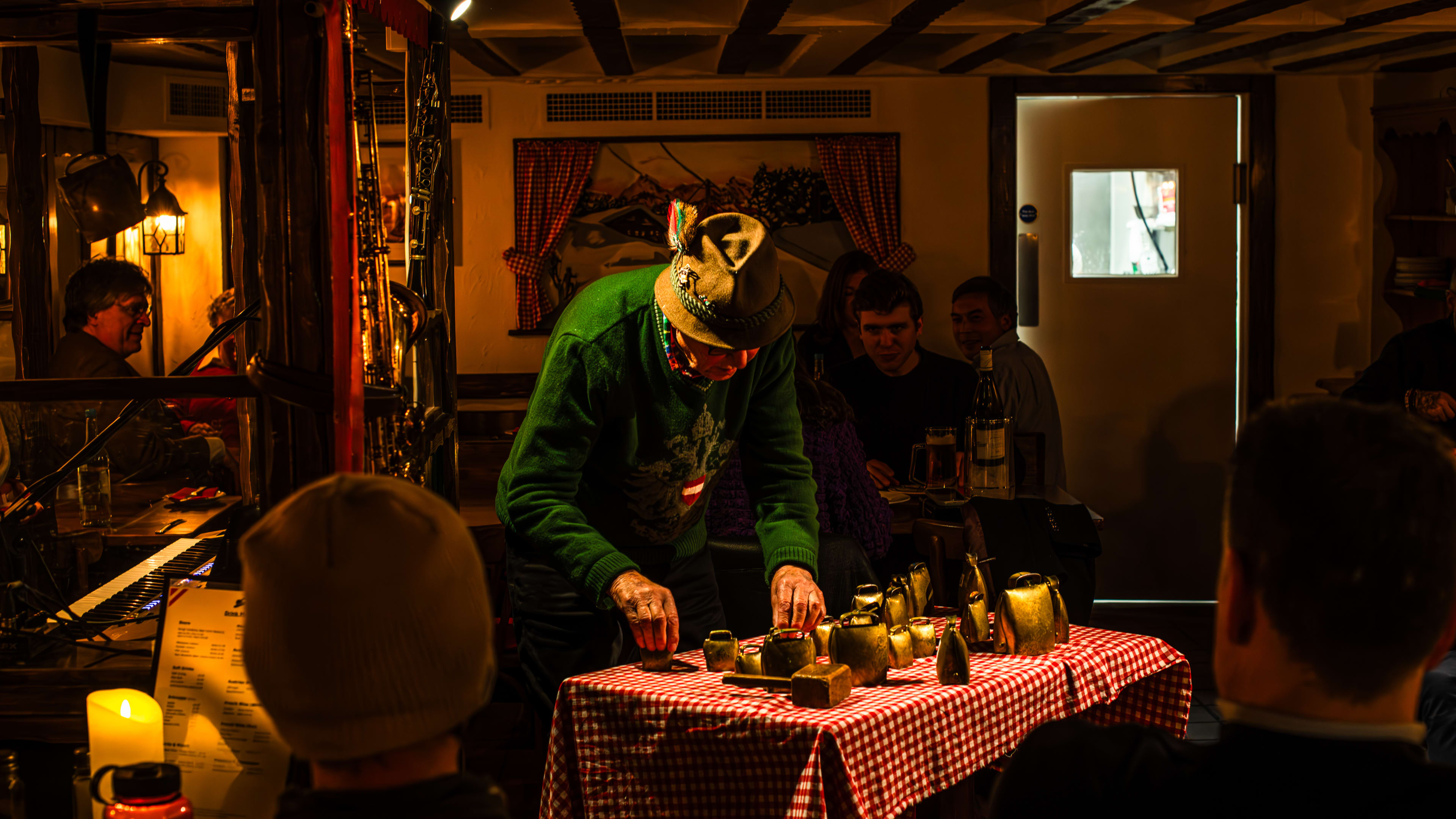 A person performing with cowbells at a table with a gingham table cloth inside The Tiroler Hut with people watching.