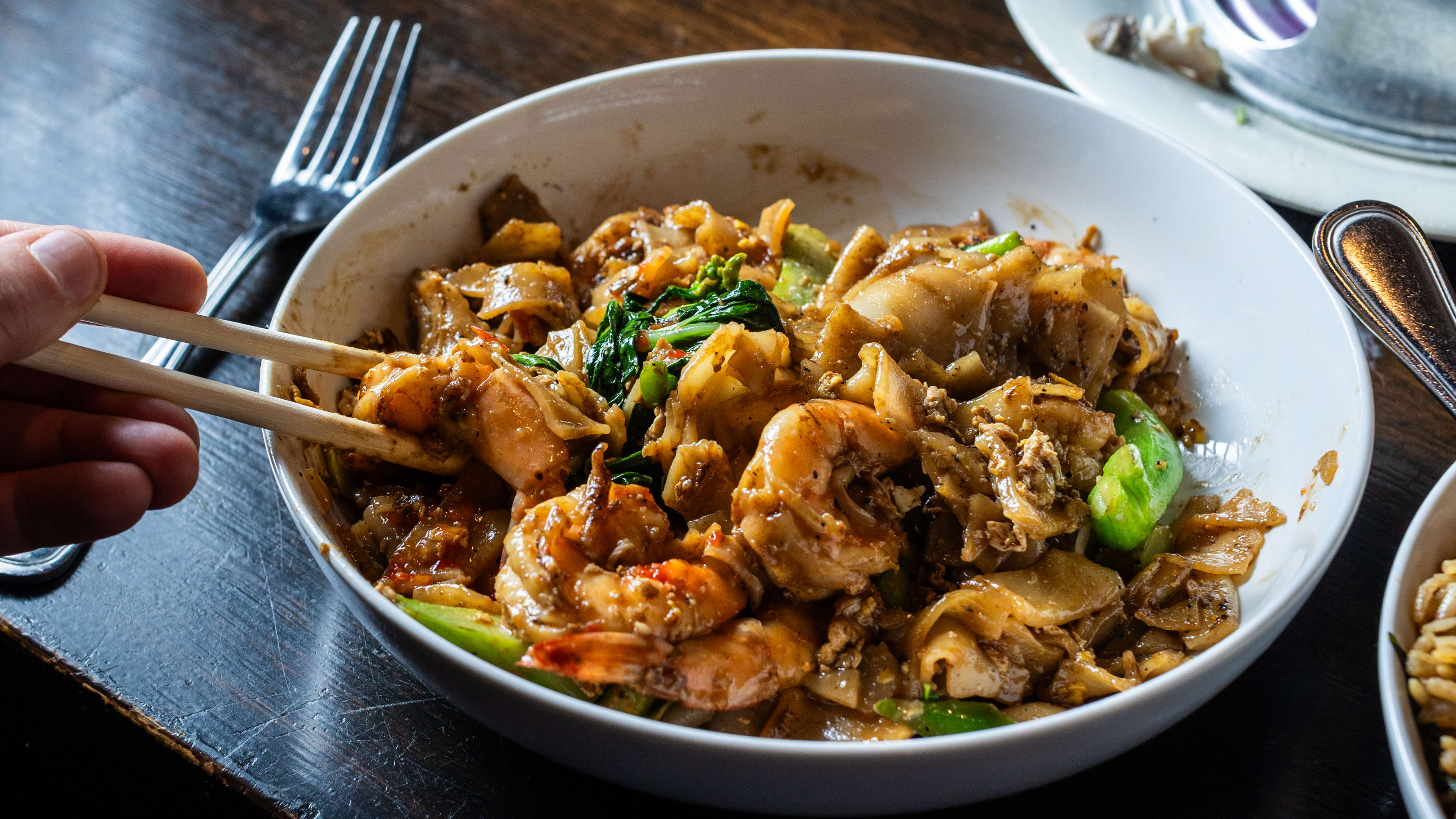 A person digs into the pad see ew with shrimp with their chopsticks.