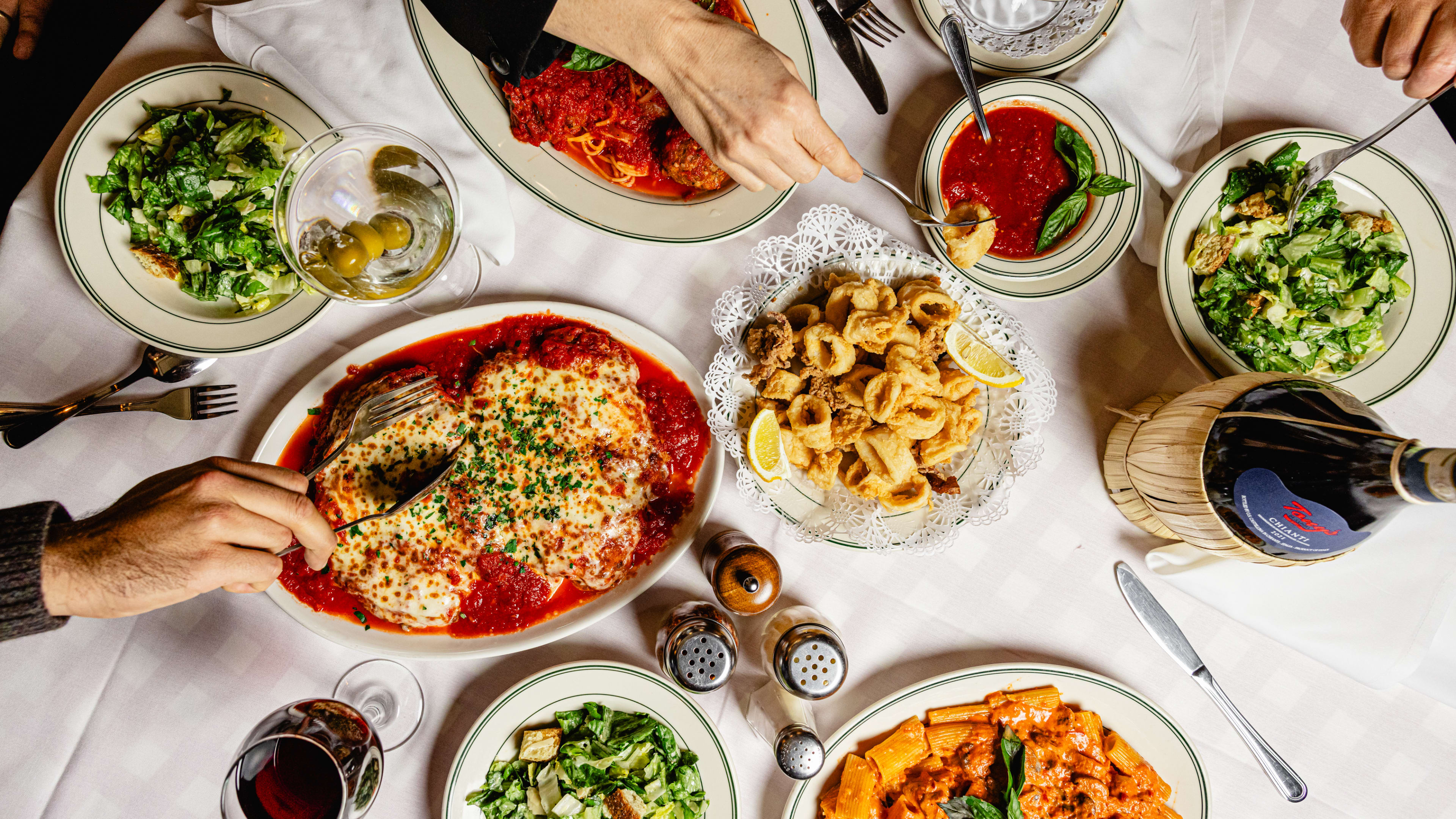 A top-down view of table covered in pasta, salad, chicken parm, red wine, and frito misto.