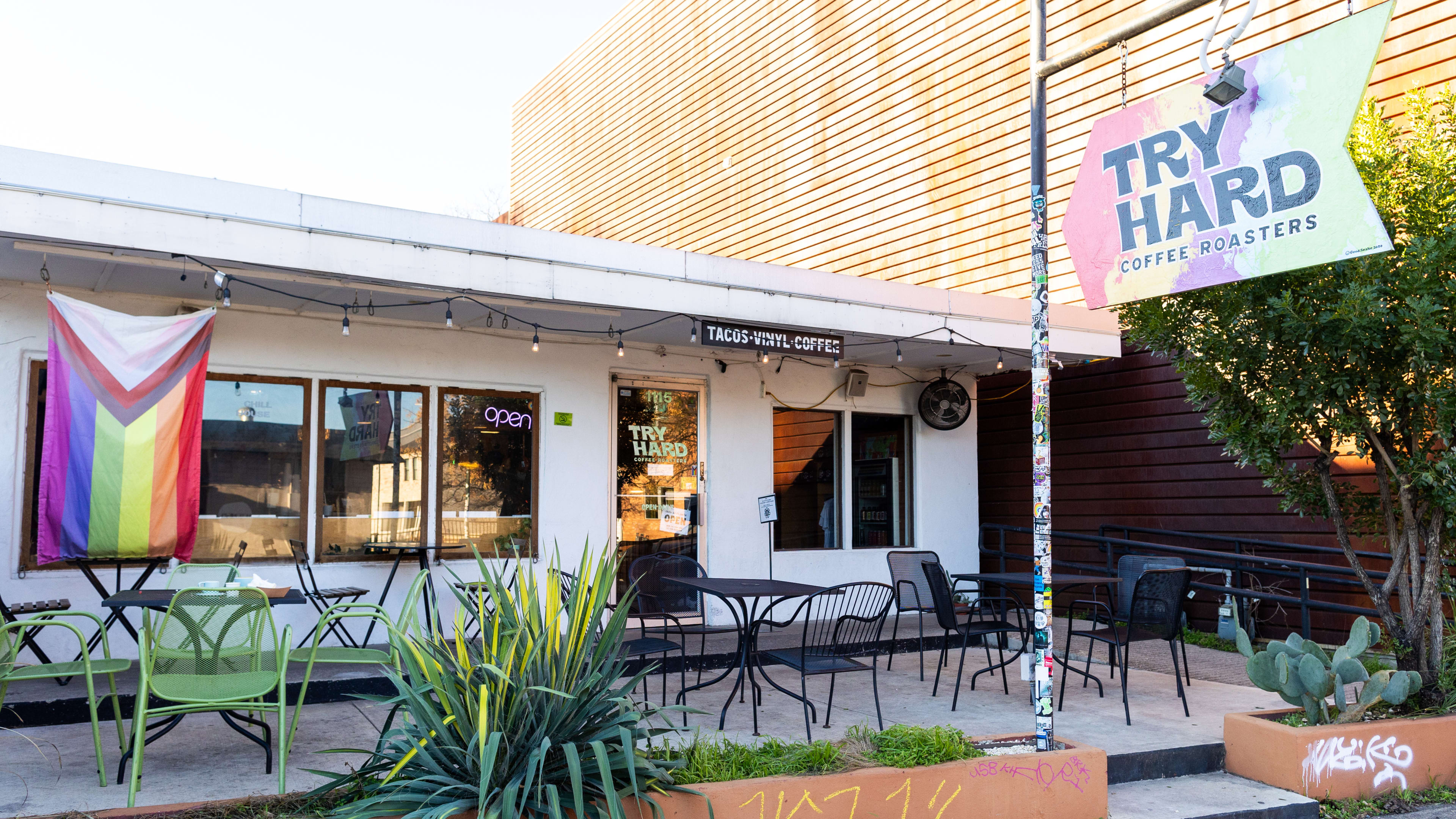 The entrance to Try Hard Coffee with patio seating out front, a LGBTQIA+ flag hanging on the front and a rainbow sign.