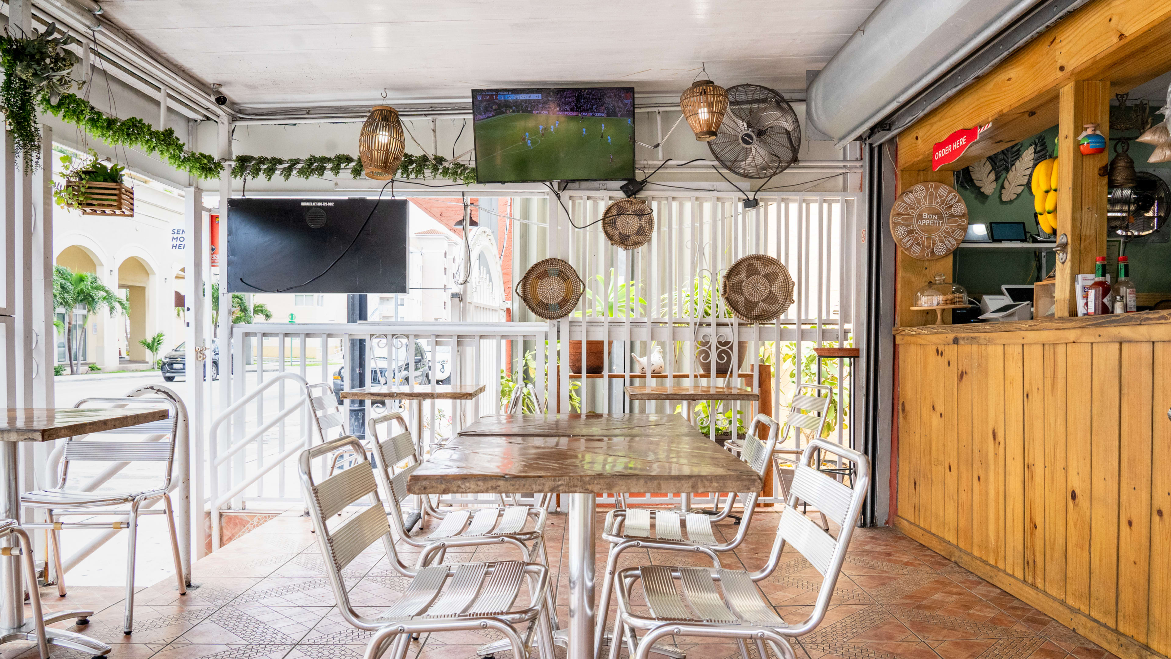 Outdoor restaurant with wooden tables, metal chairs, wood paneling, and a tv playing soccer.