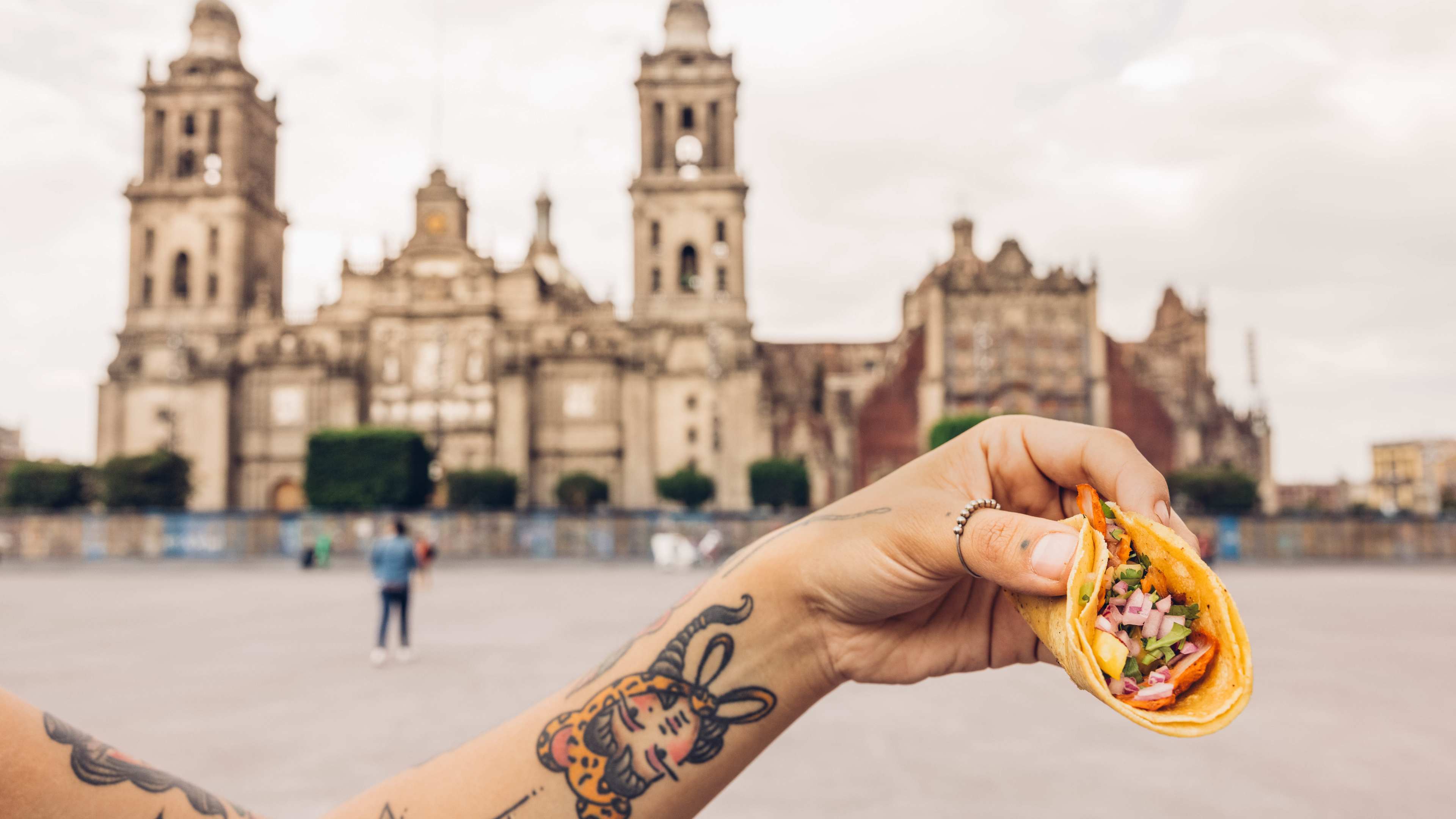 Someone holding a taco with the Zócalo in Mexico City in the background.