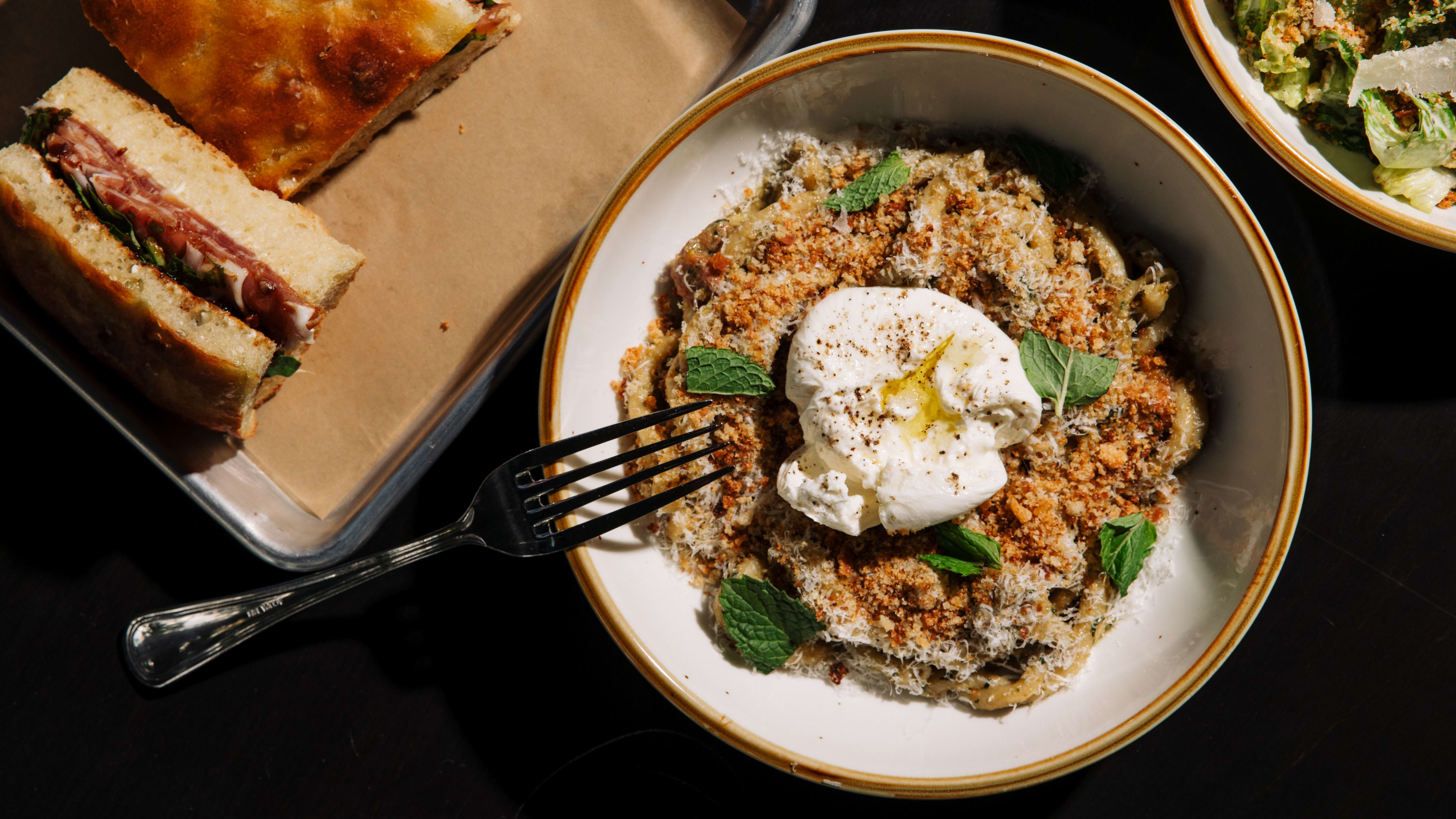 pesto pasta topped with mint leaves and burrata and a prosciutto focaccia sandwich