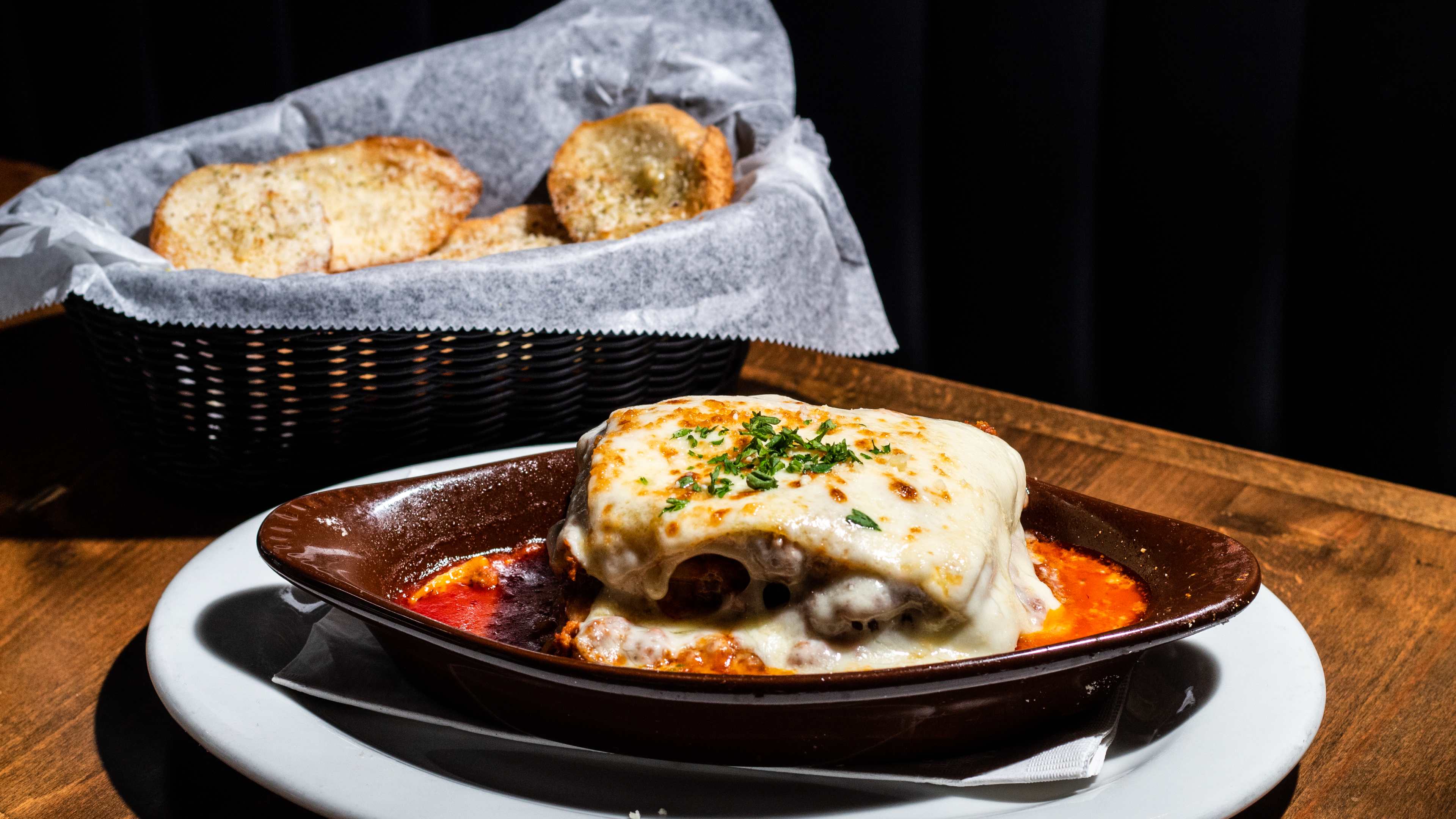 cheesy square of lasagna swimming in sauce next to bread basket