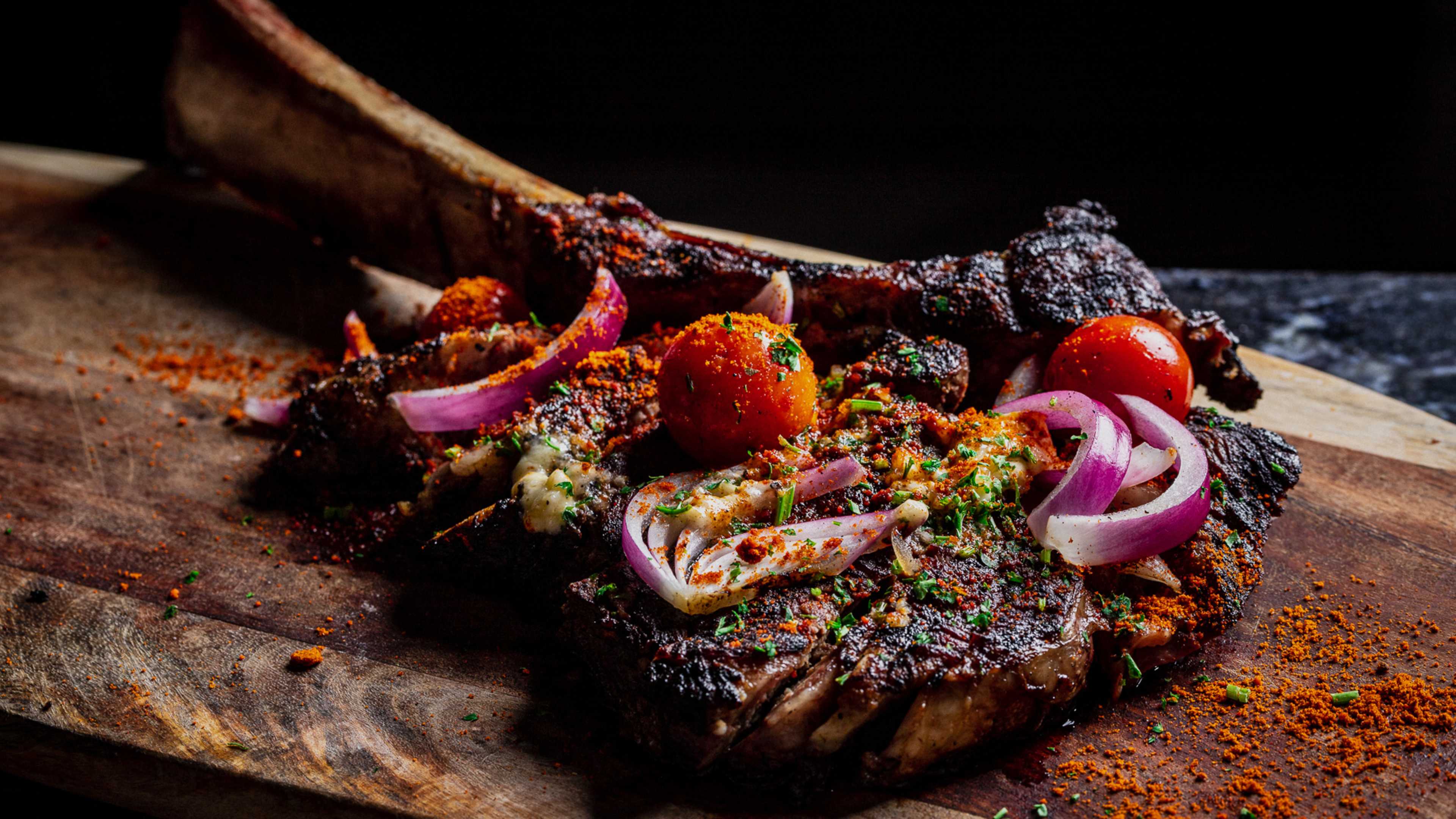 a steak on a cutting board with onions and tomatoes