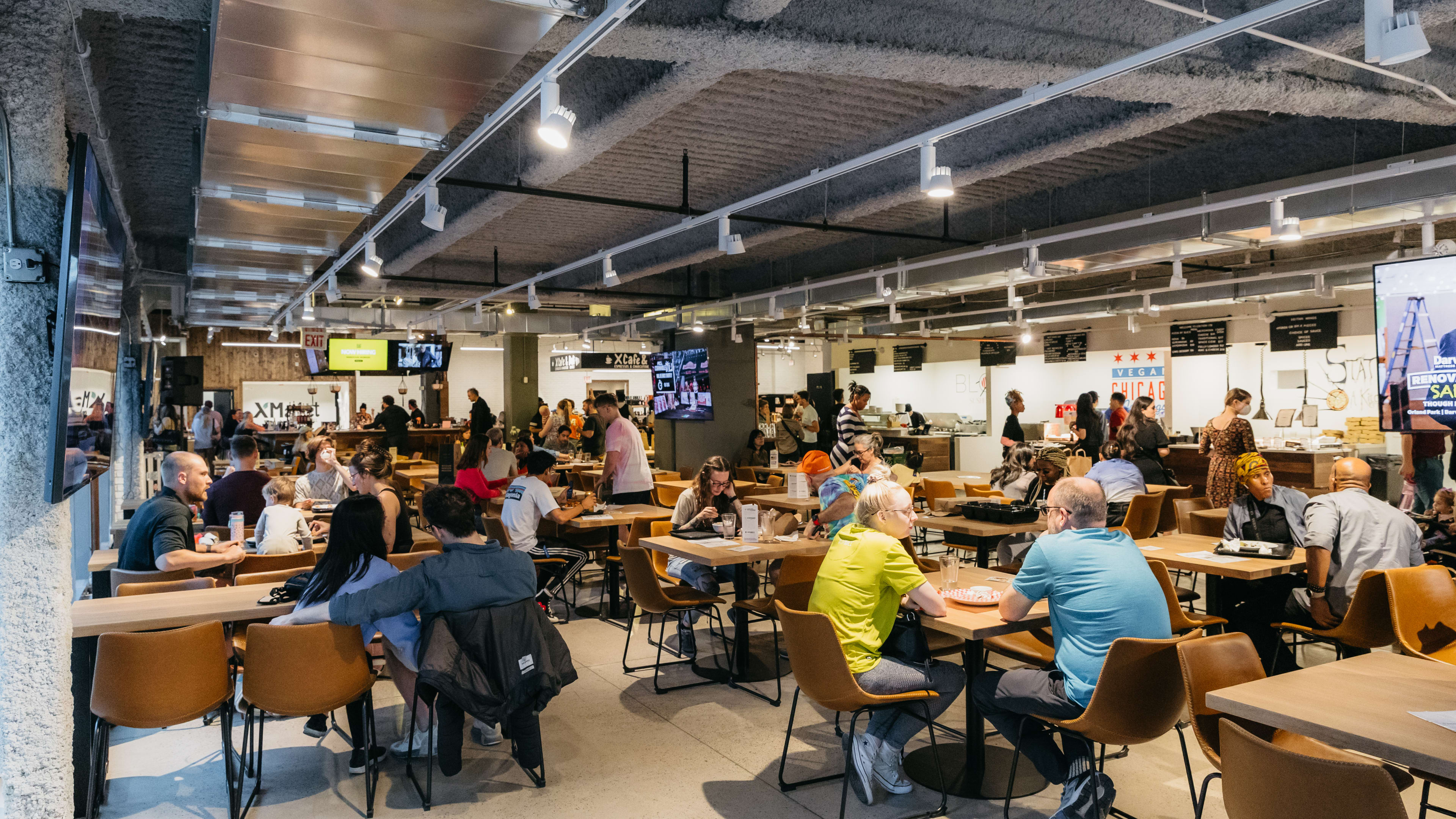 The dining area inside XMarket Food Hall. There are many tables and food stalls to order from.