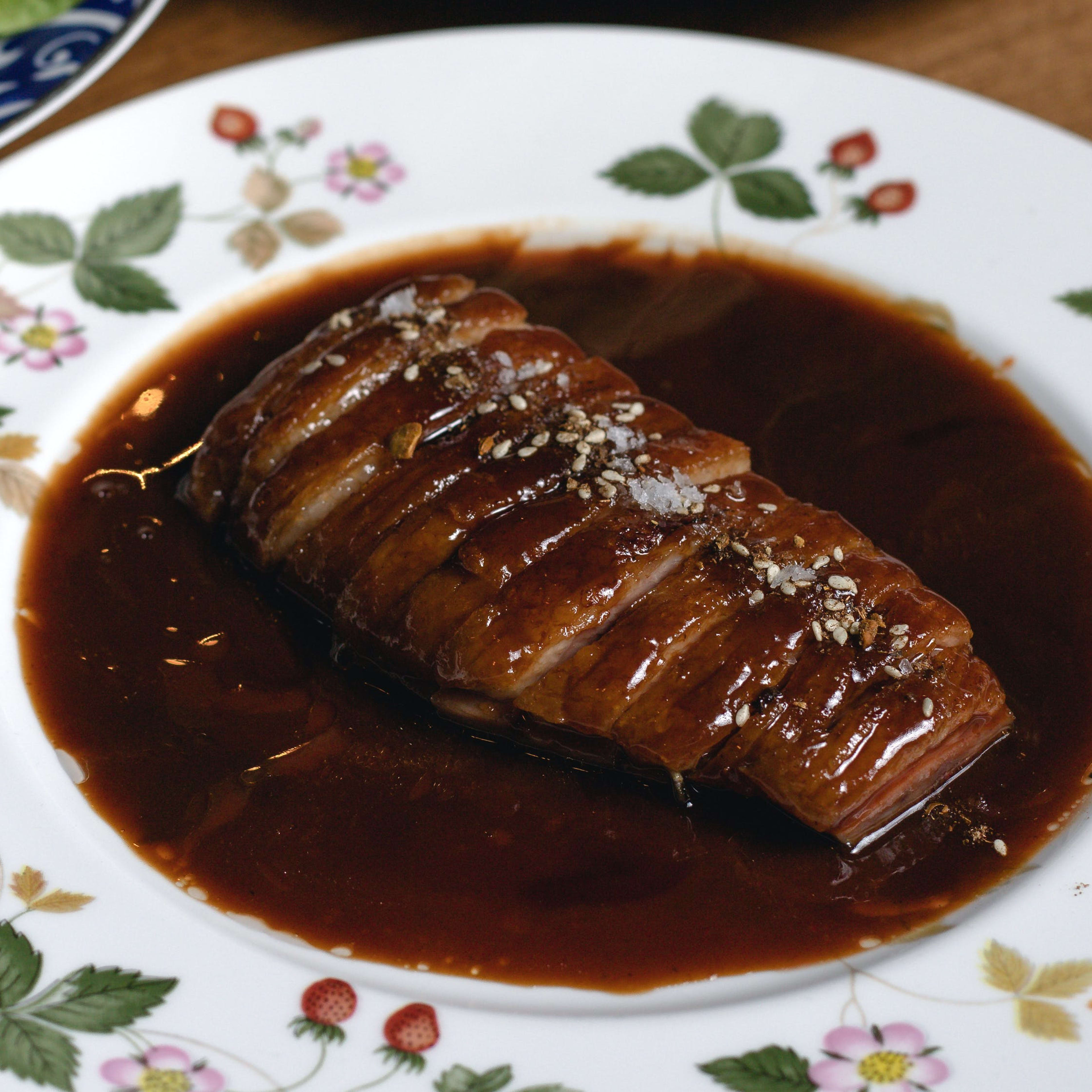 sliced duck in pool of sauce on decorative porcelain plate