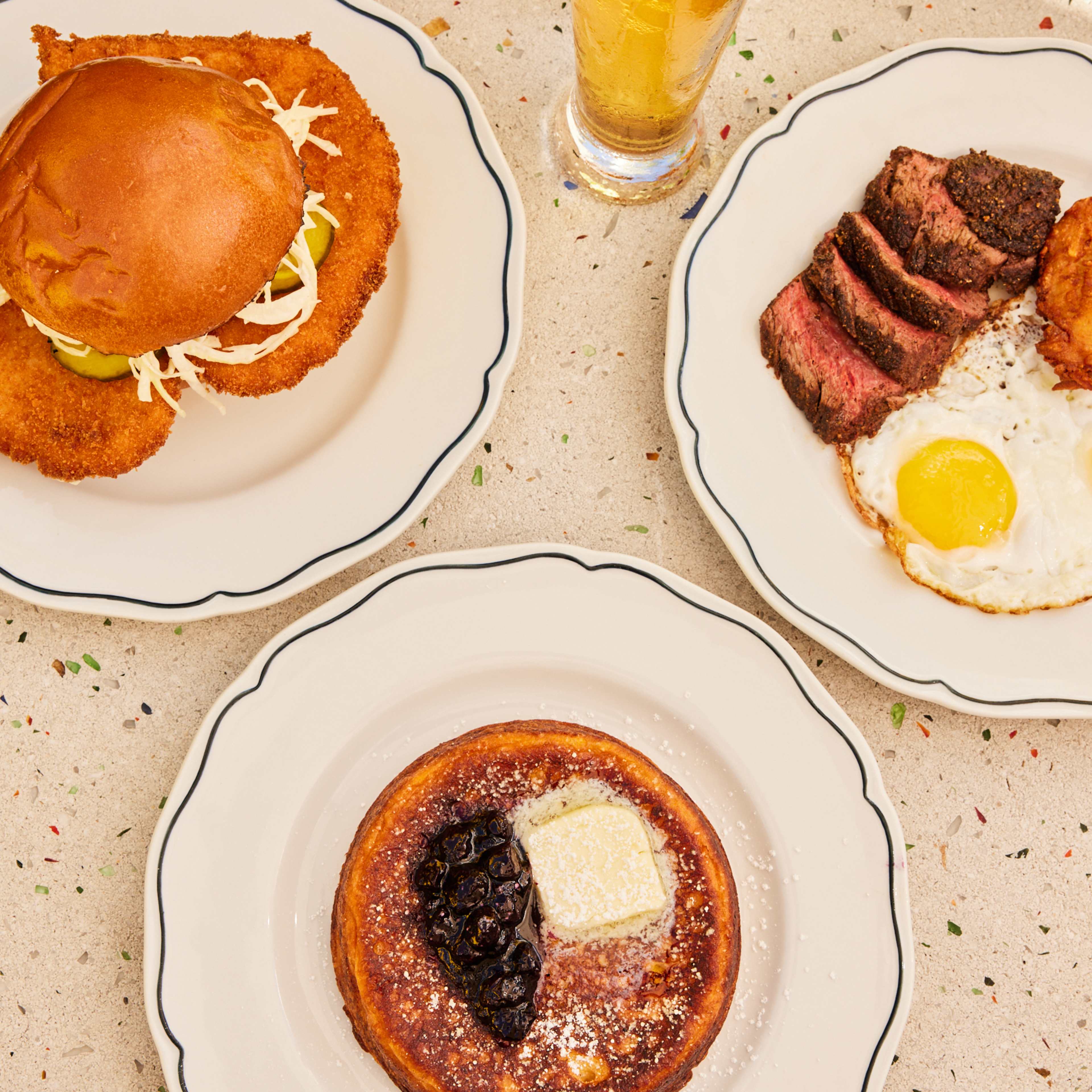 A sandwich, steak and eggs, and a pancake on a table.