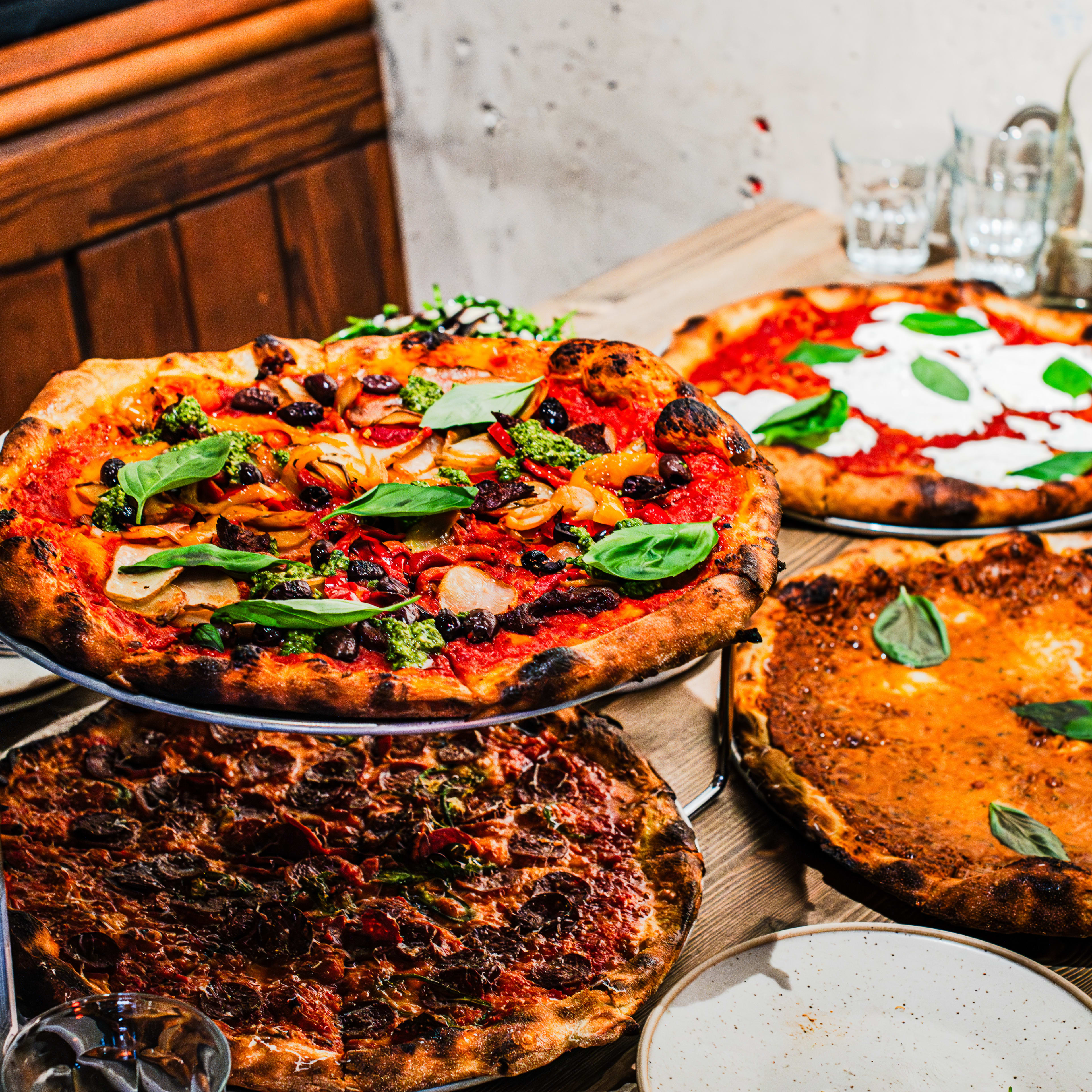 Four thin-crust pizzas on a table with a wooden booth in the background.